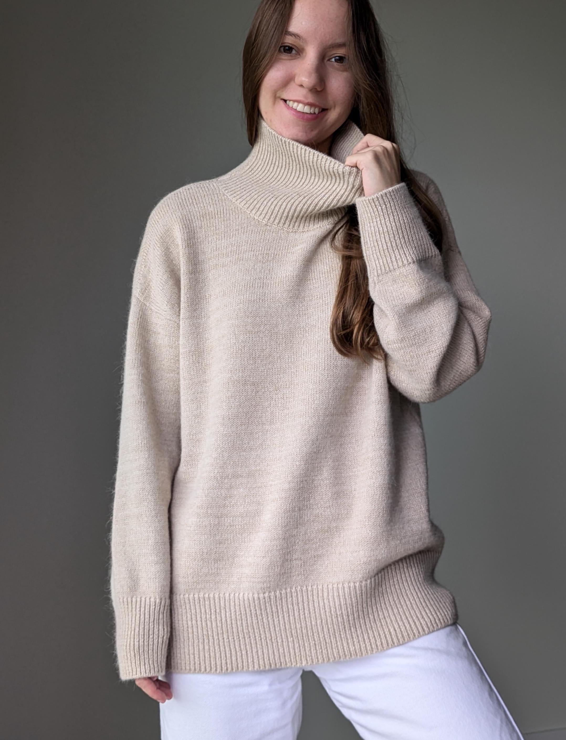 Sand woman wearing a beige turtleneck sweater against a gray background