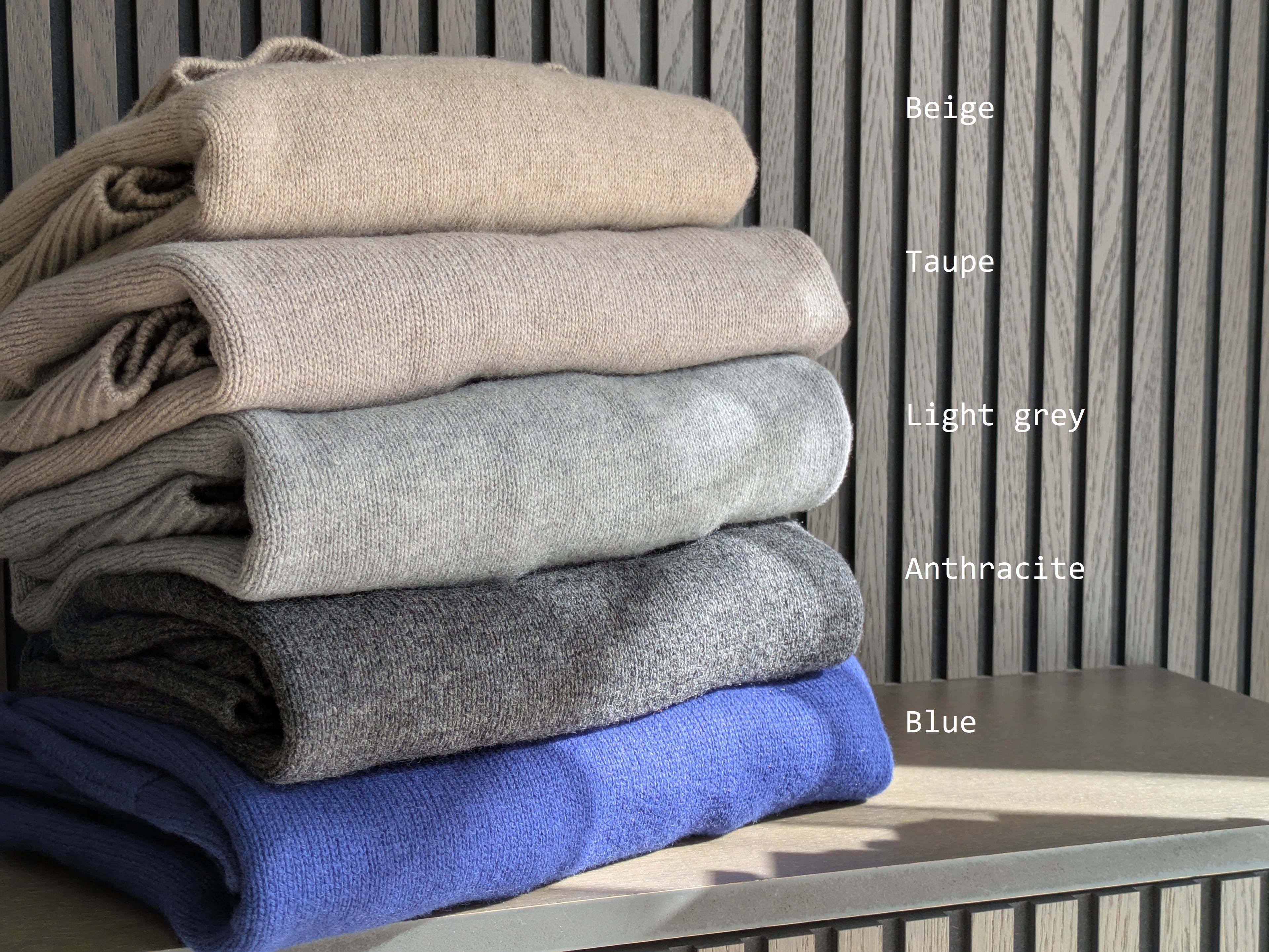 Anthracite Stack of folded cloths in beige, taupe, light gray, anthracite, and blue on a wooden surface with color labels.