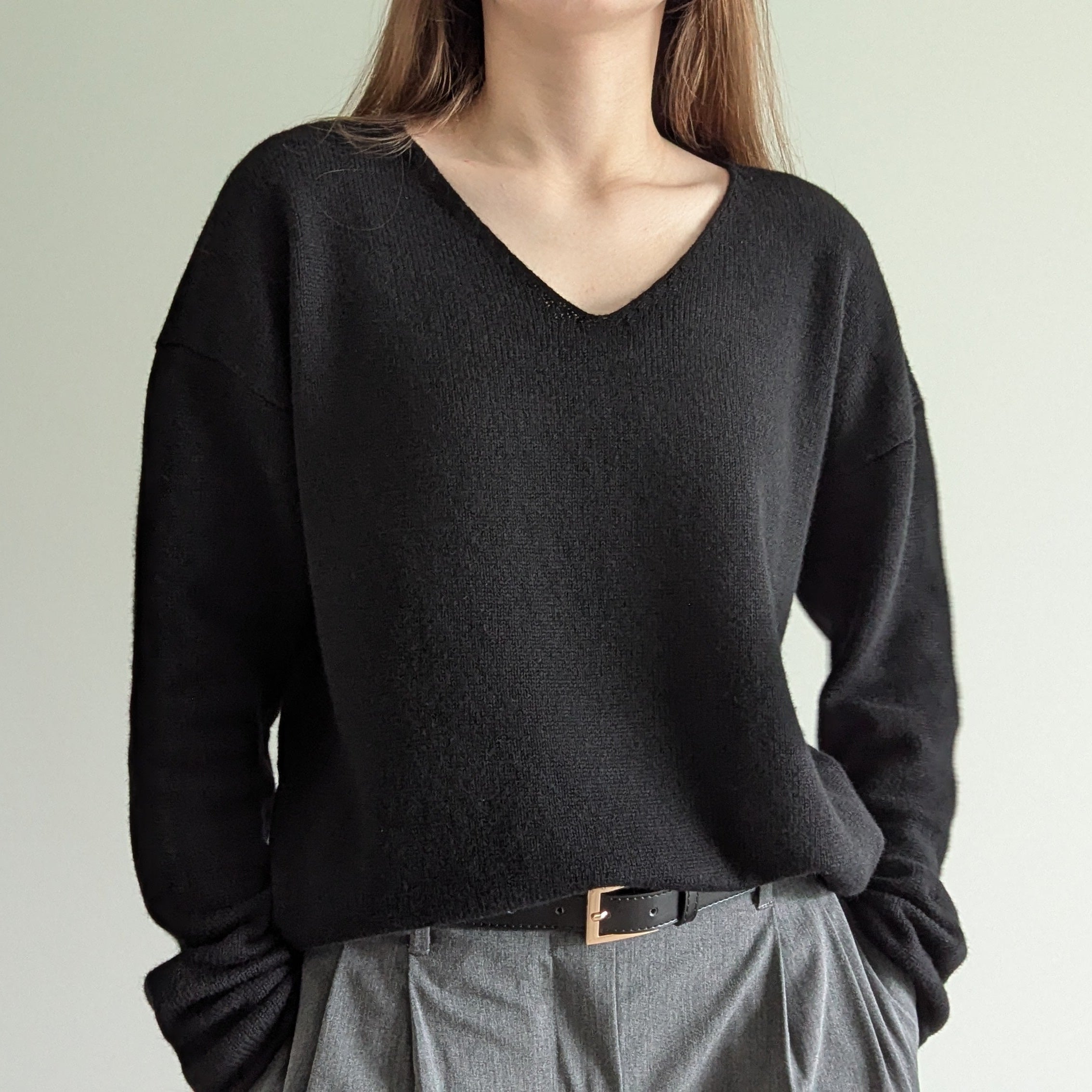 Black Person wearing a black sweater and gray pants against a plain background