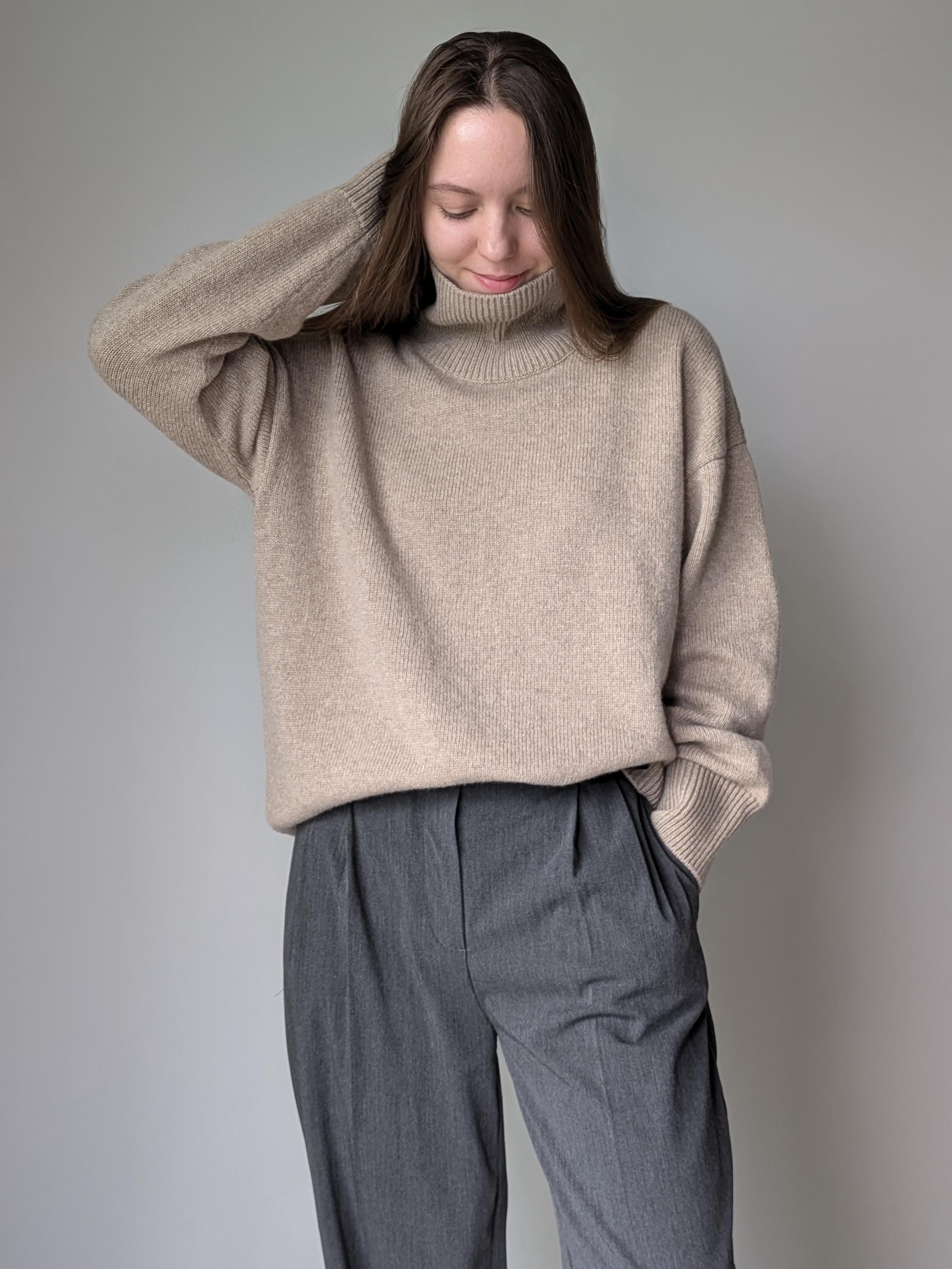 Beige Person wearing a beige sweater and gray pants against a plain background