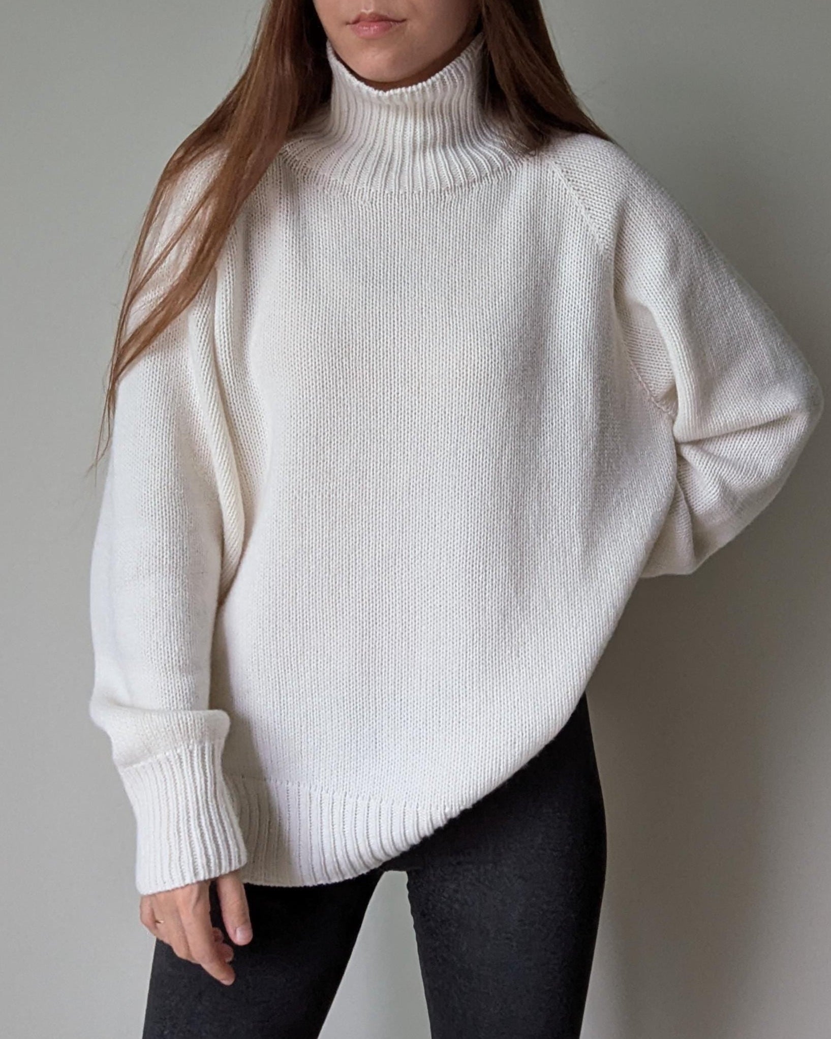 White Person wearing a white turtleneck sweater against a plain background
