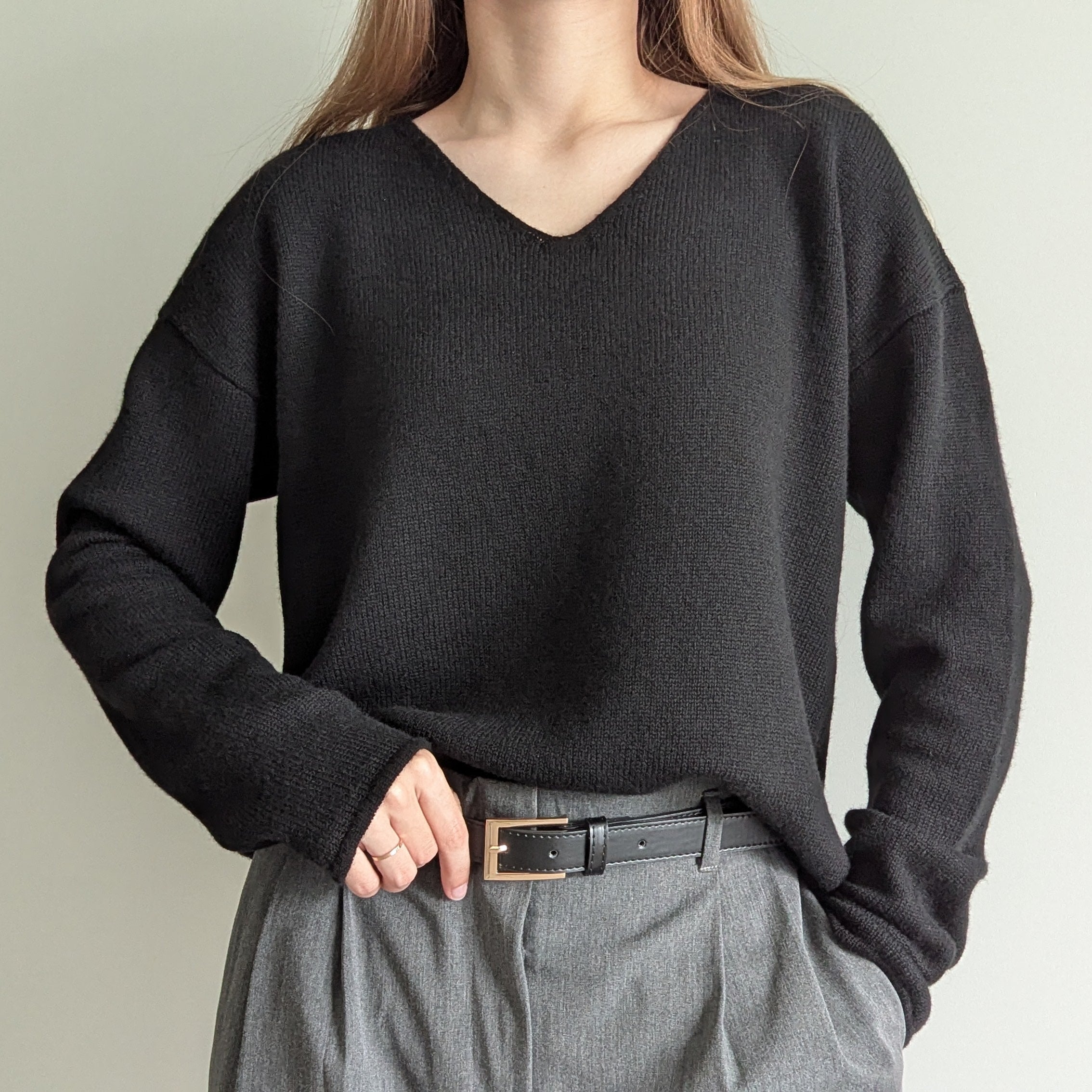 Black Person wearing a black sweater and gray pants against a plain background