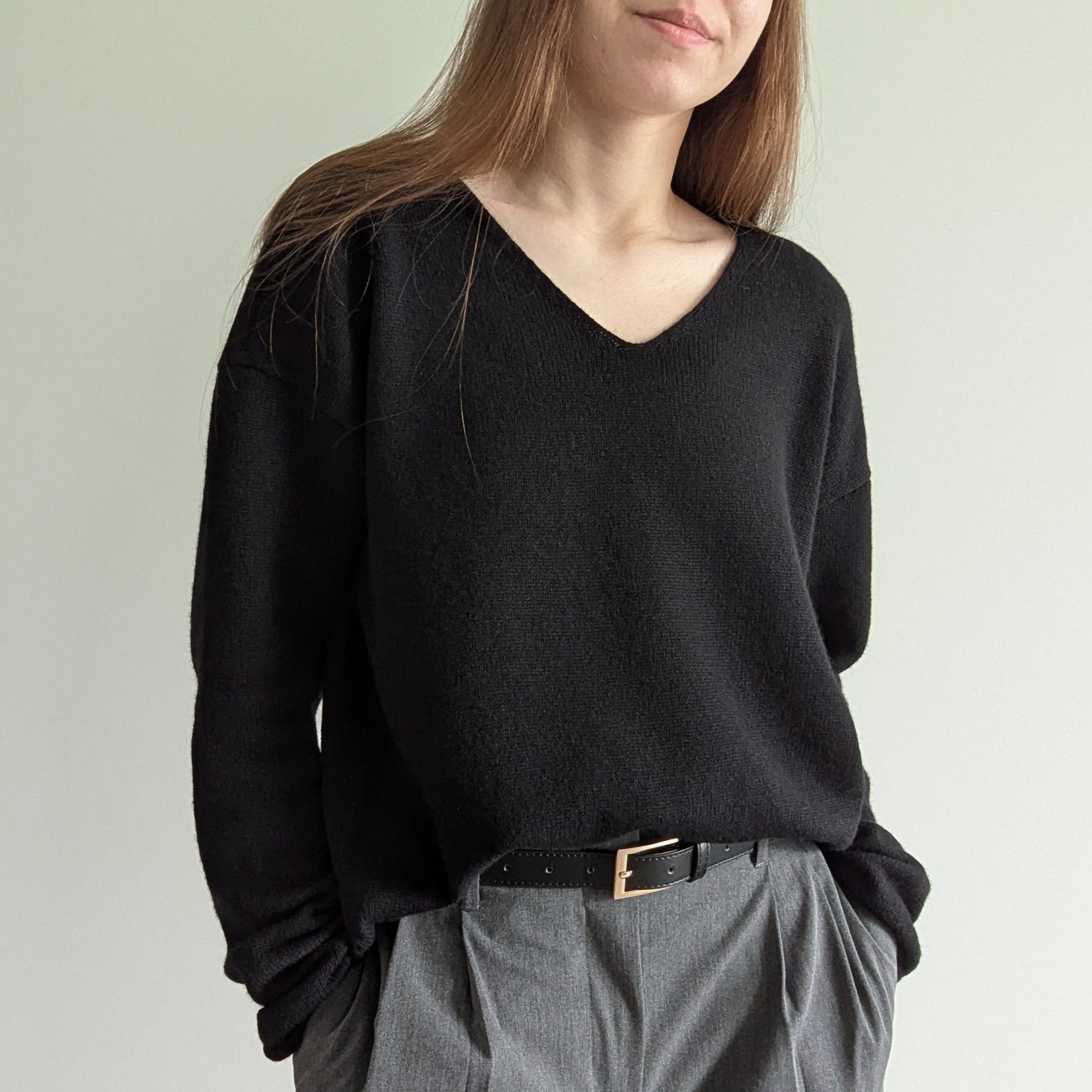 Black Person wearing a black sweater and gray pants against a plain background