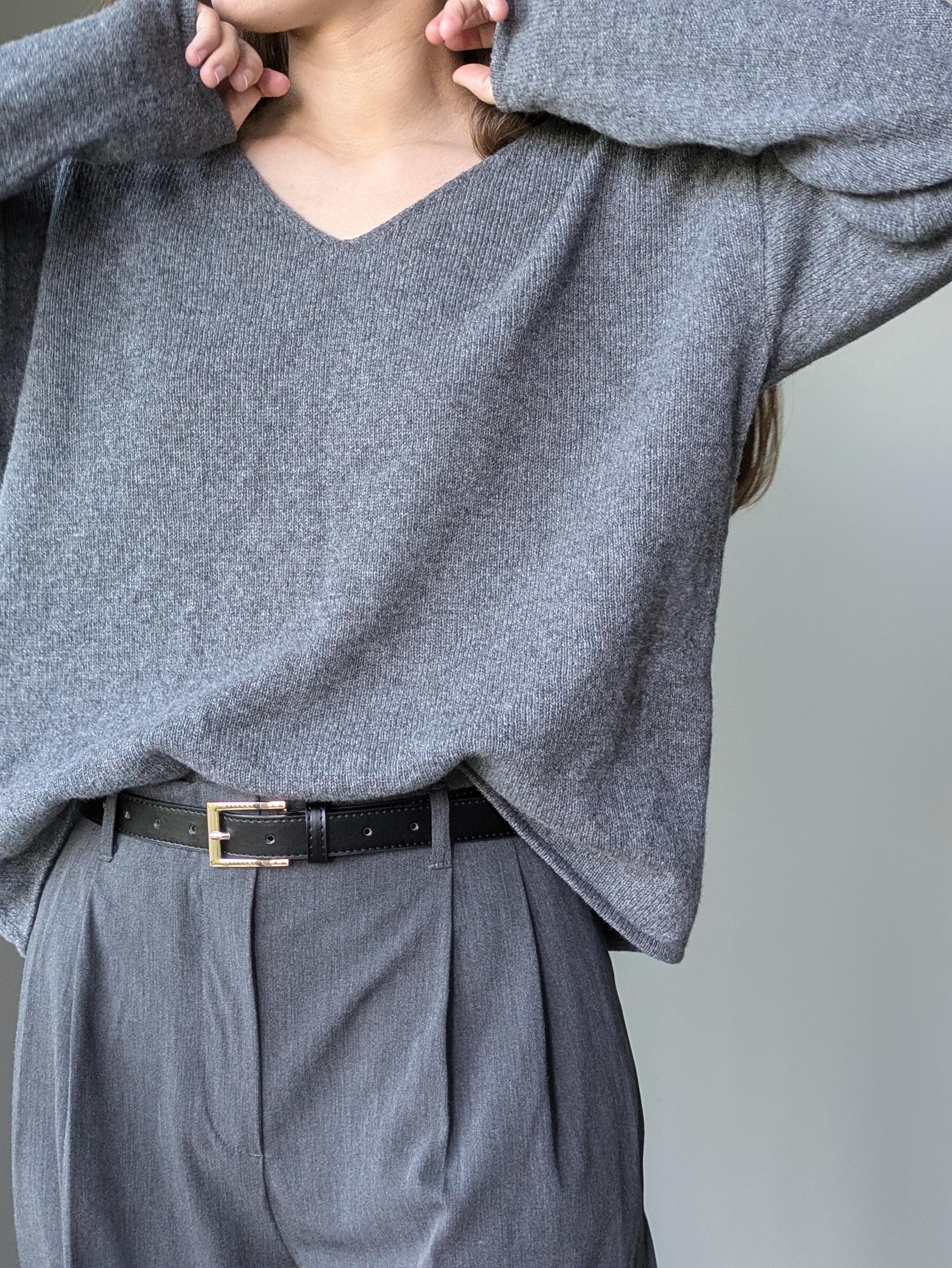 Gray Person wearing a gray sweater and pants with a belt against a neutral background