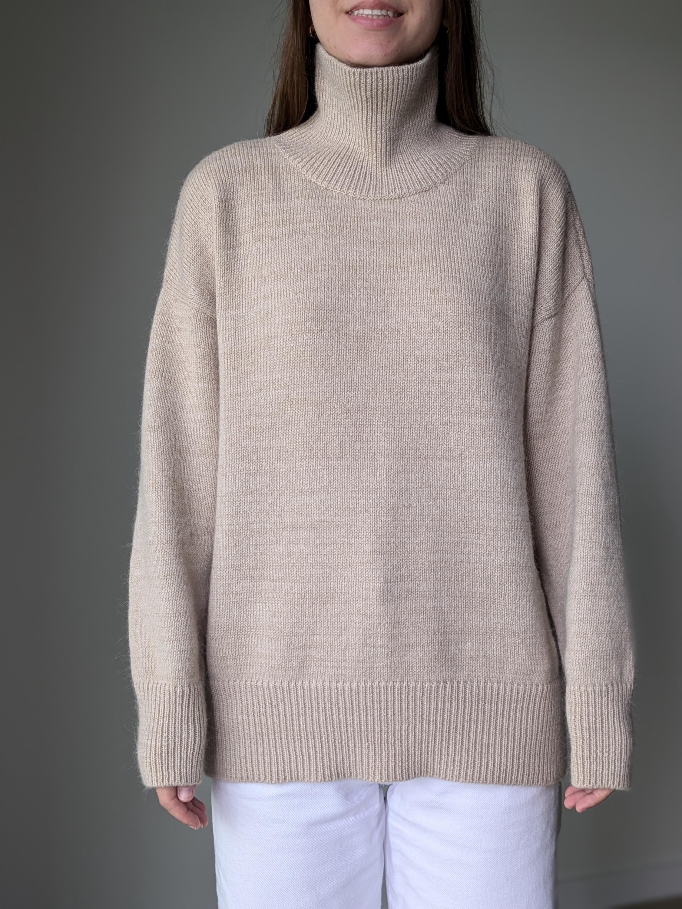 Sand person wearing a beige turtleneck sweater against a gray background