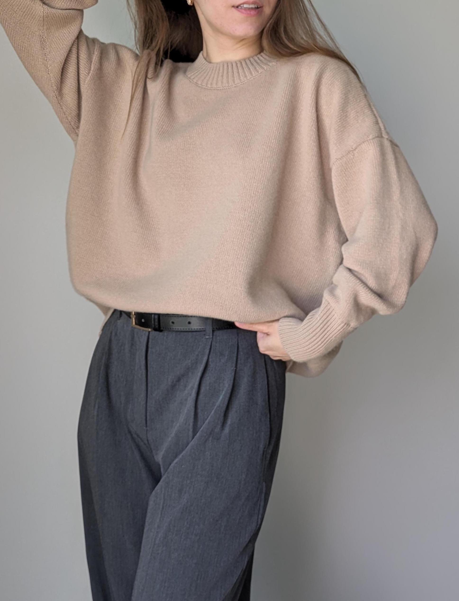 Person wearing a beige sweater and gray pants against a plain background