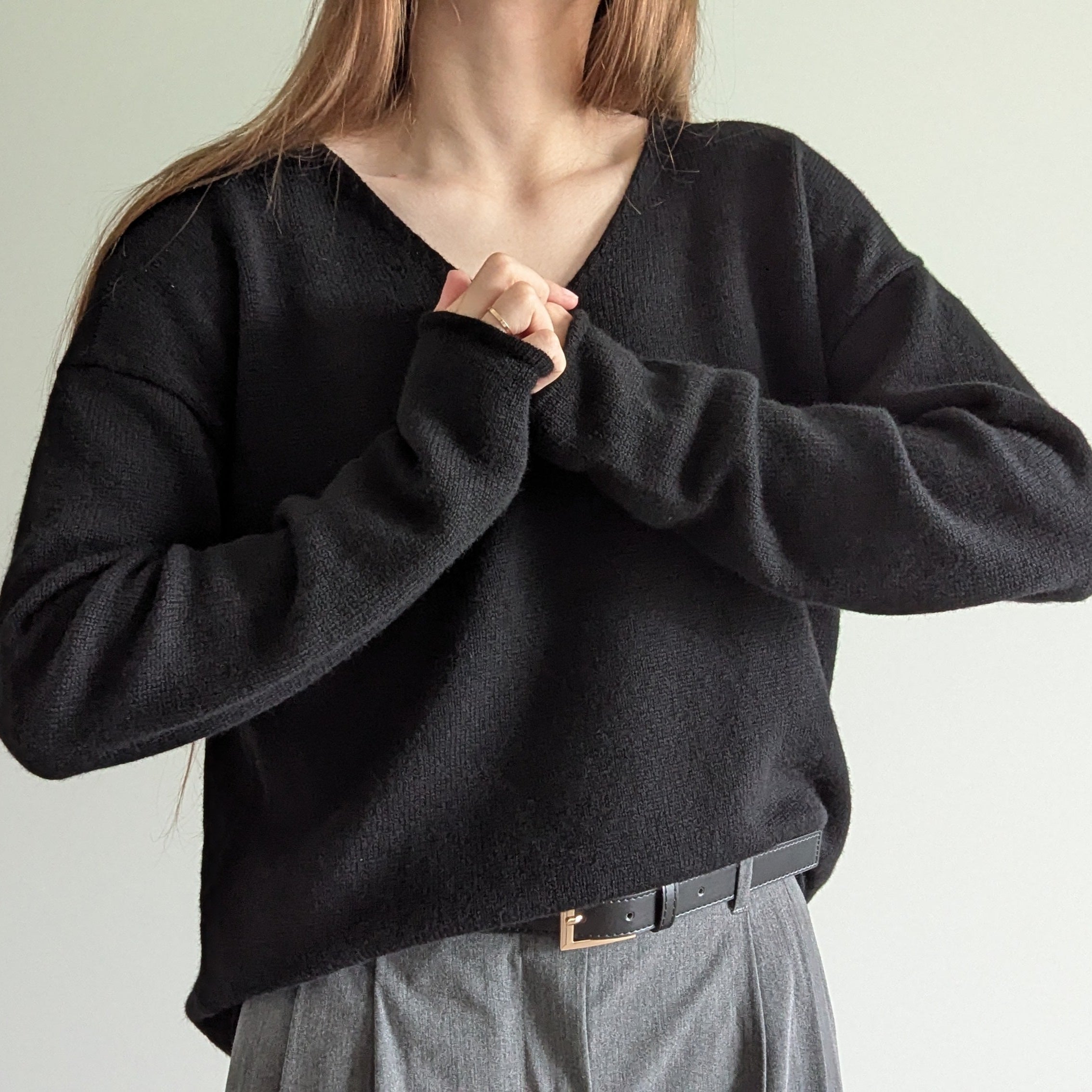 Black Person wearing a black sweater and gray pants against a plain background
