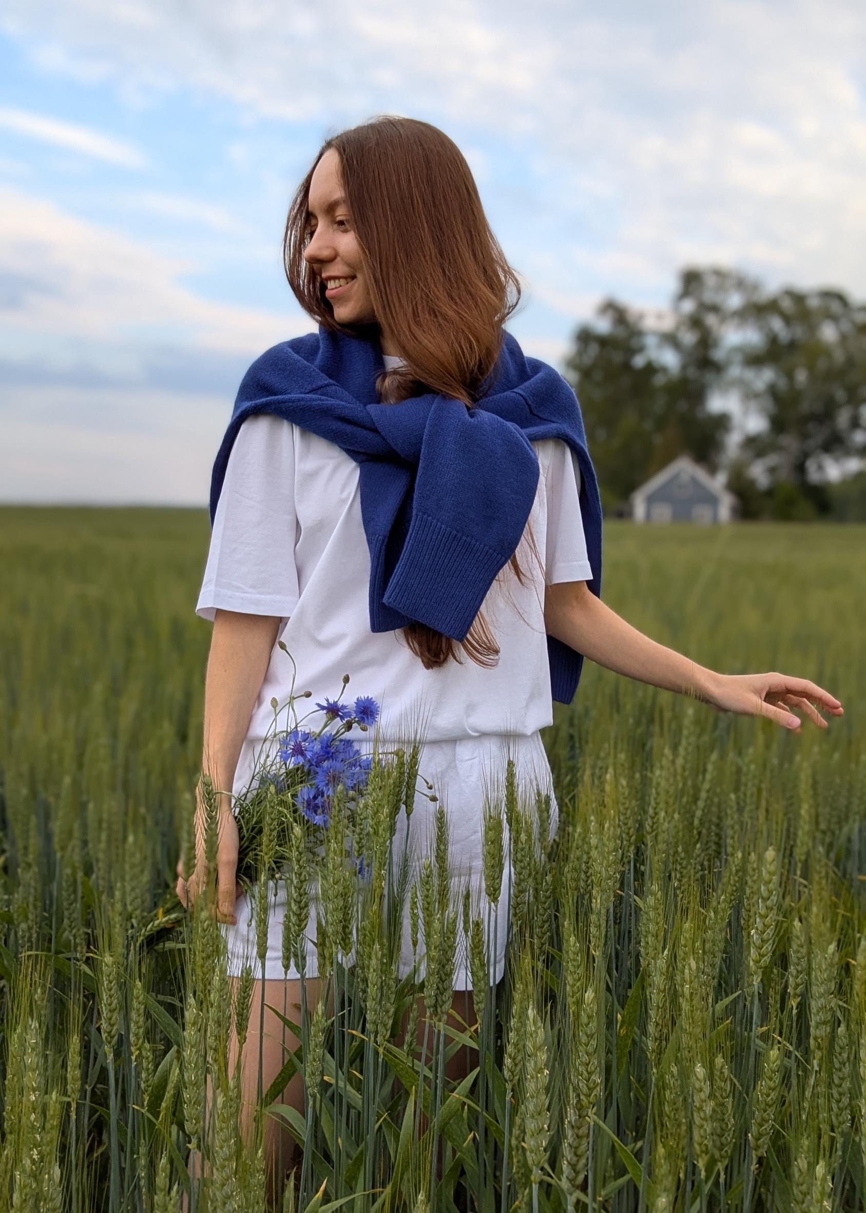 Blue merino cashmere sweater casually draped over the shoulders with sleeves tied around the neck, showcasing a relaxed yet stylish look.