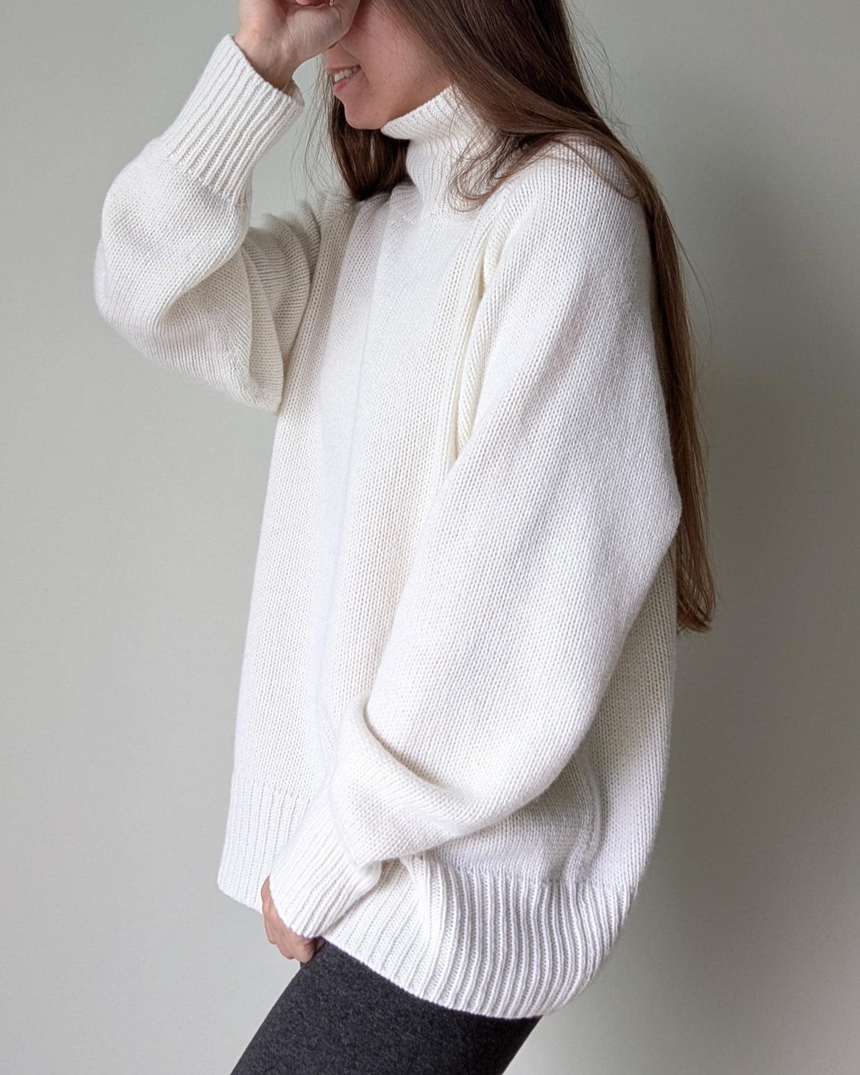 White Person wearing a white sweater against a plain background