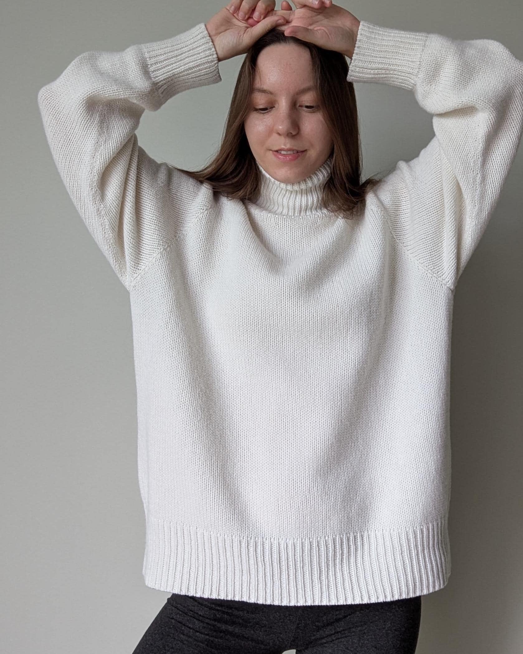 White Person wearing a white sweater against a plain background