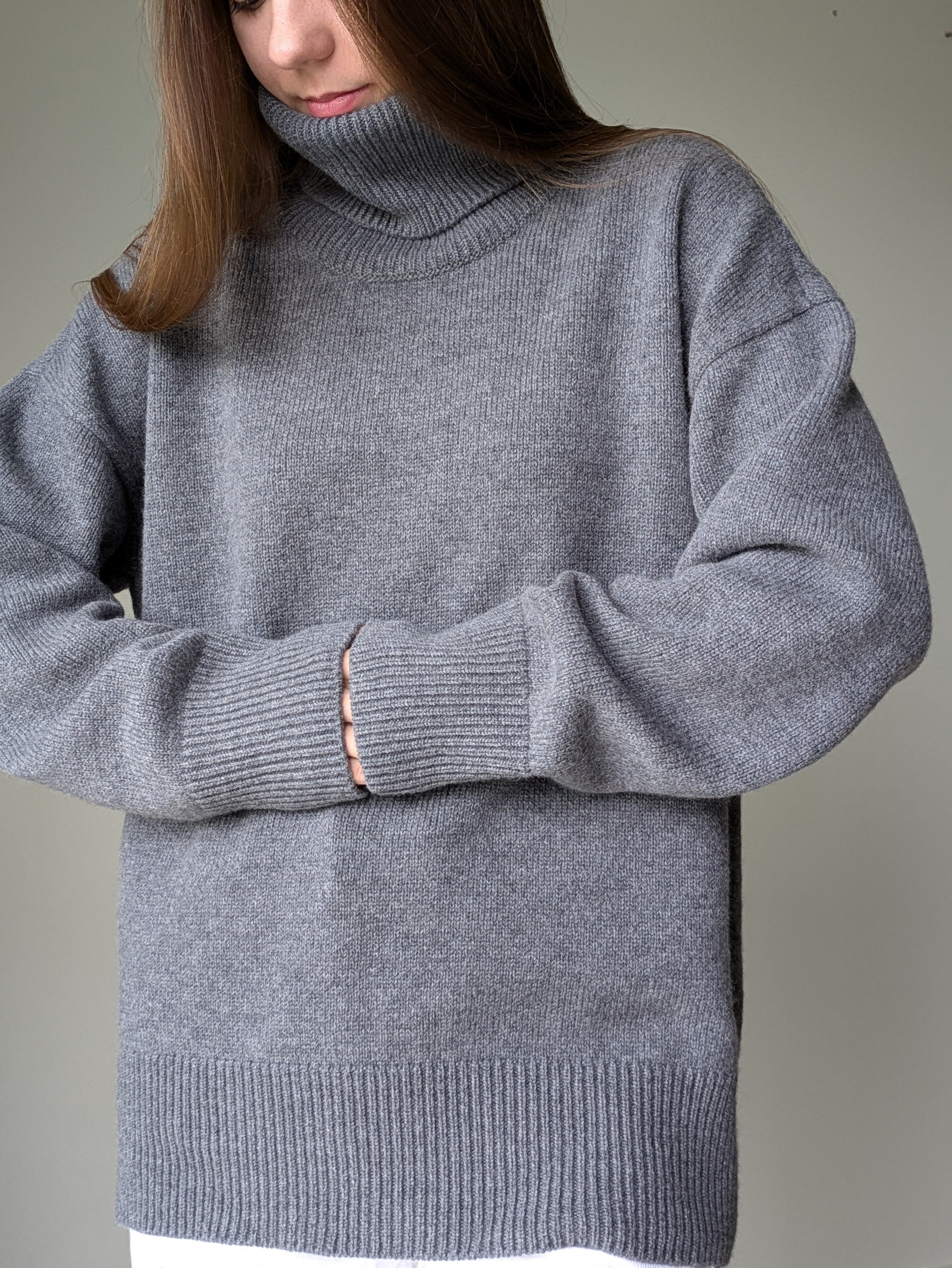 Gray Person wearing a gray turtleneck sweater against a neutral background