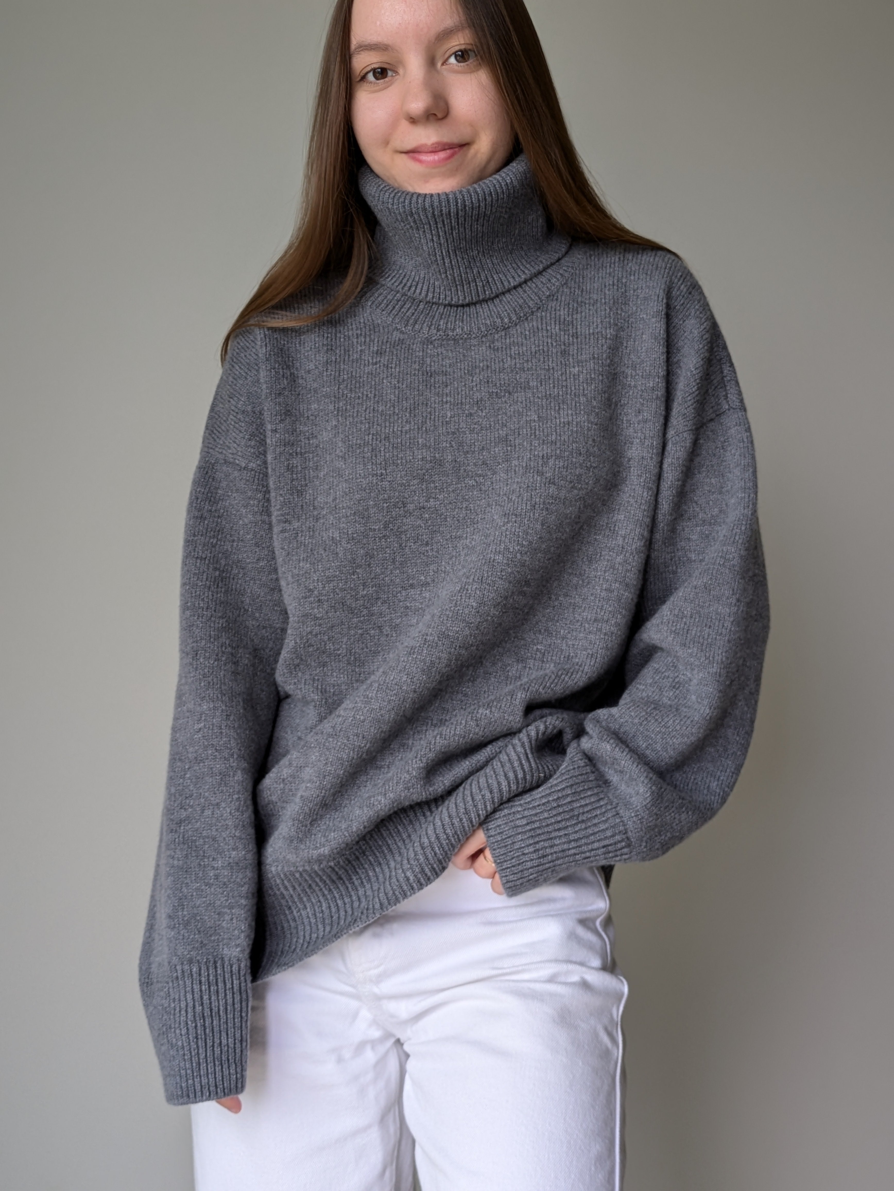 Gray Person wearing a gray turtleneck sweater and white pants against a plain background