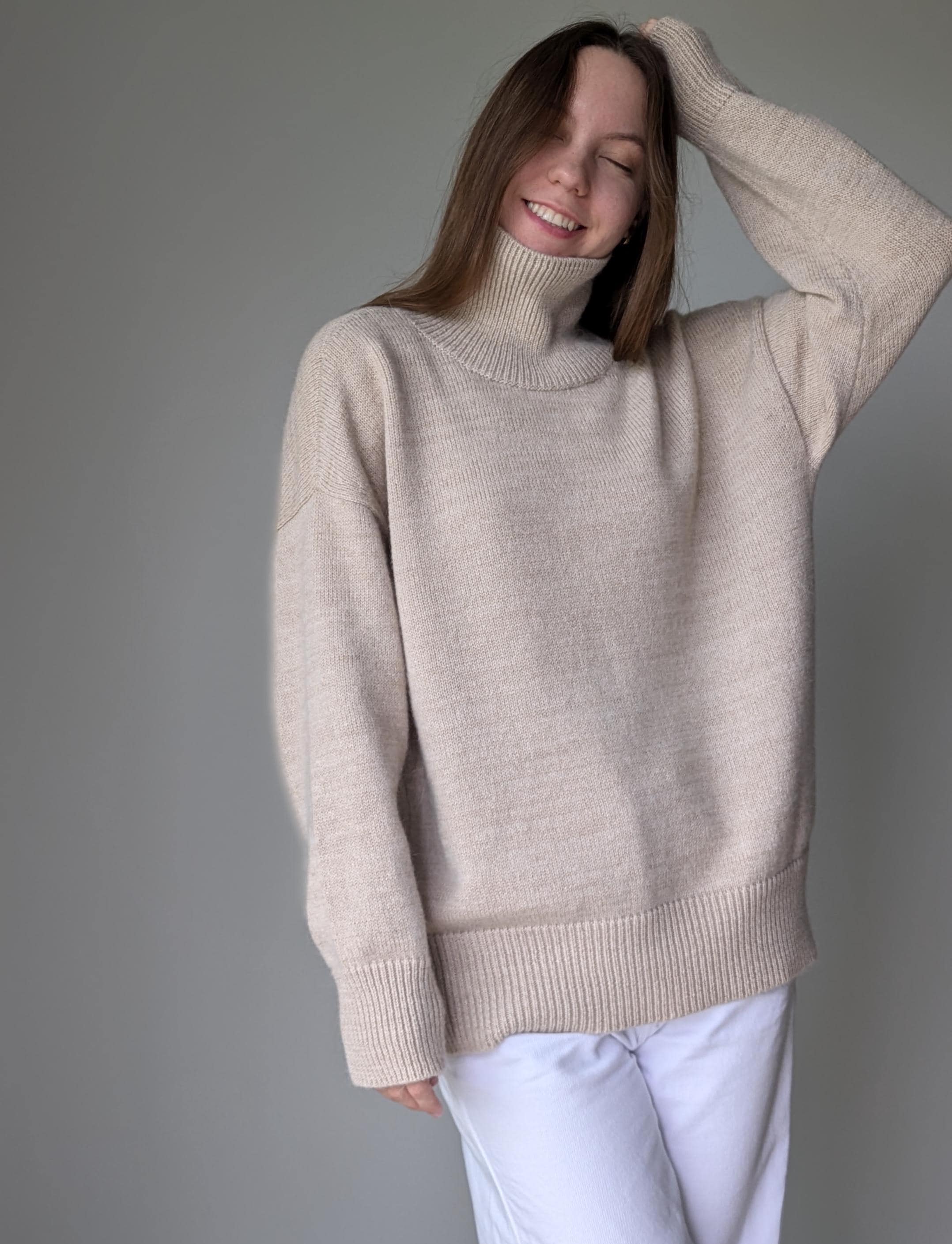 Sand woman wearing a beige sweater against a gray background