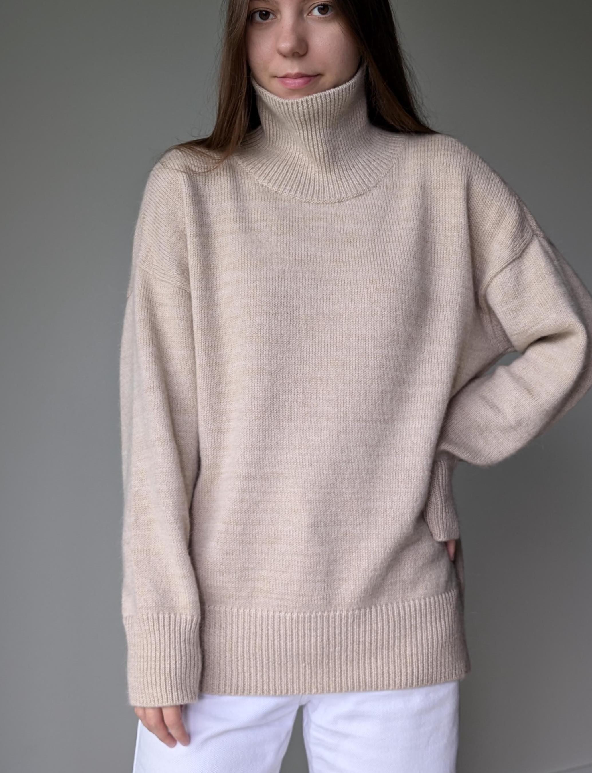 Sand person wearing a beige turtleneck sweater against a gray background