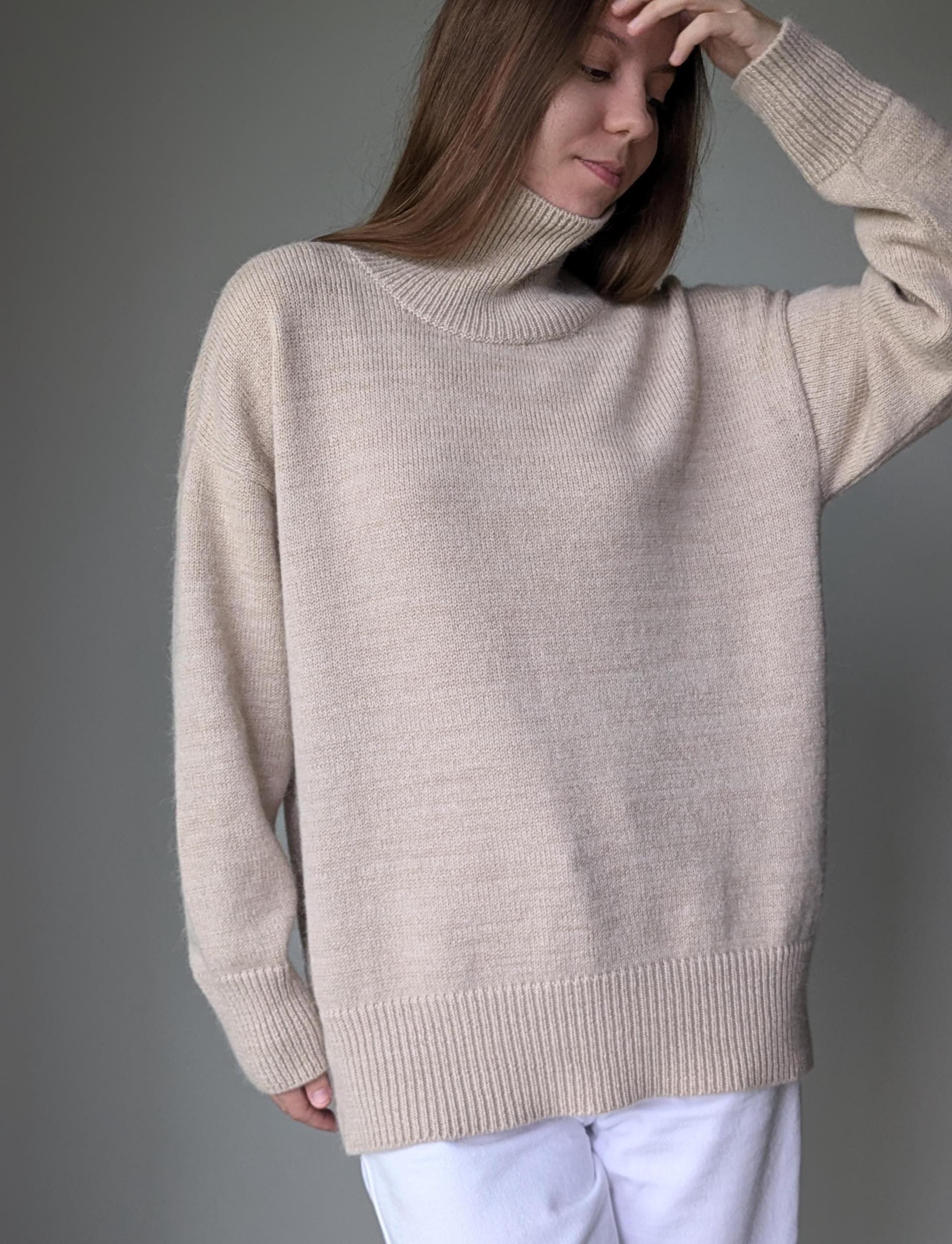 Sand woman wearing a beige sweater against a gray background