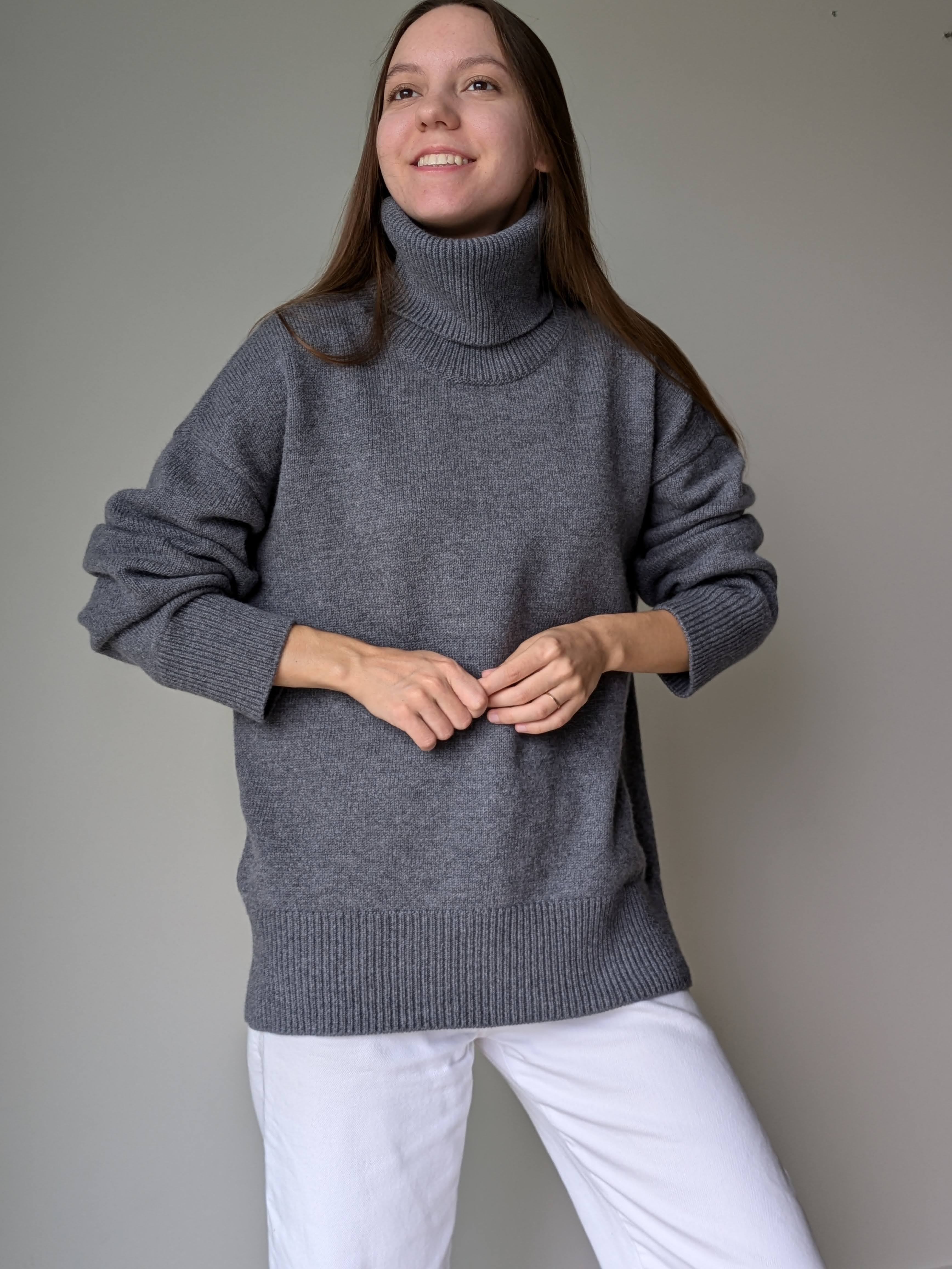 Gray Person wearing a gray turtleneck sweater and white pants against a plain background