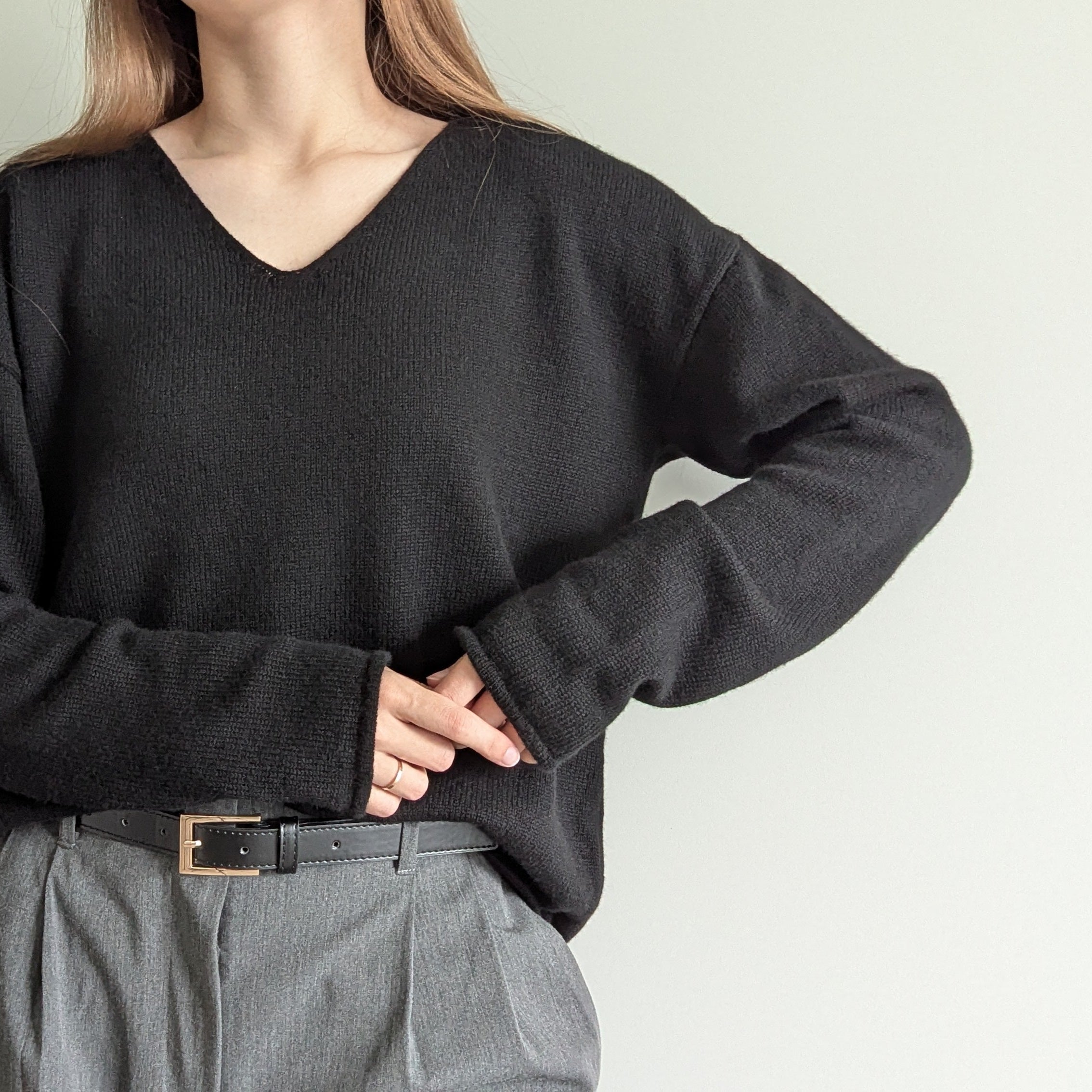 Black Person wearing a black sweater and gray pants against a plain background