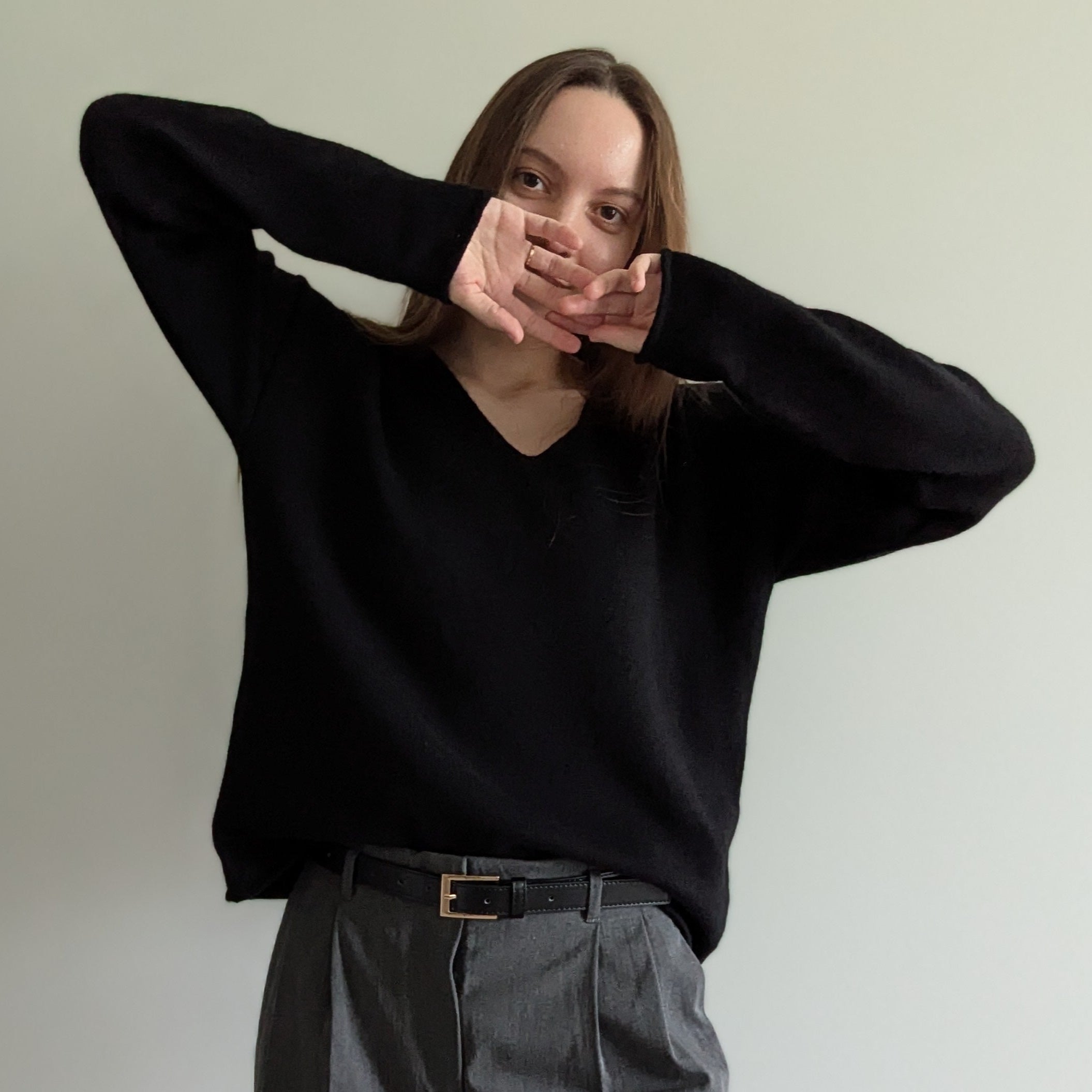 Black Person wearing a black sweater and gray pants against a plain background