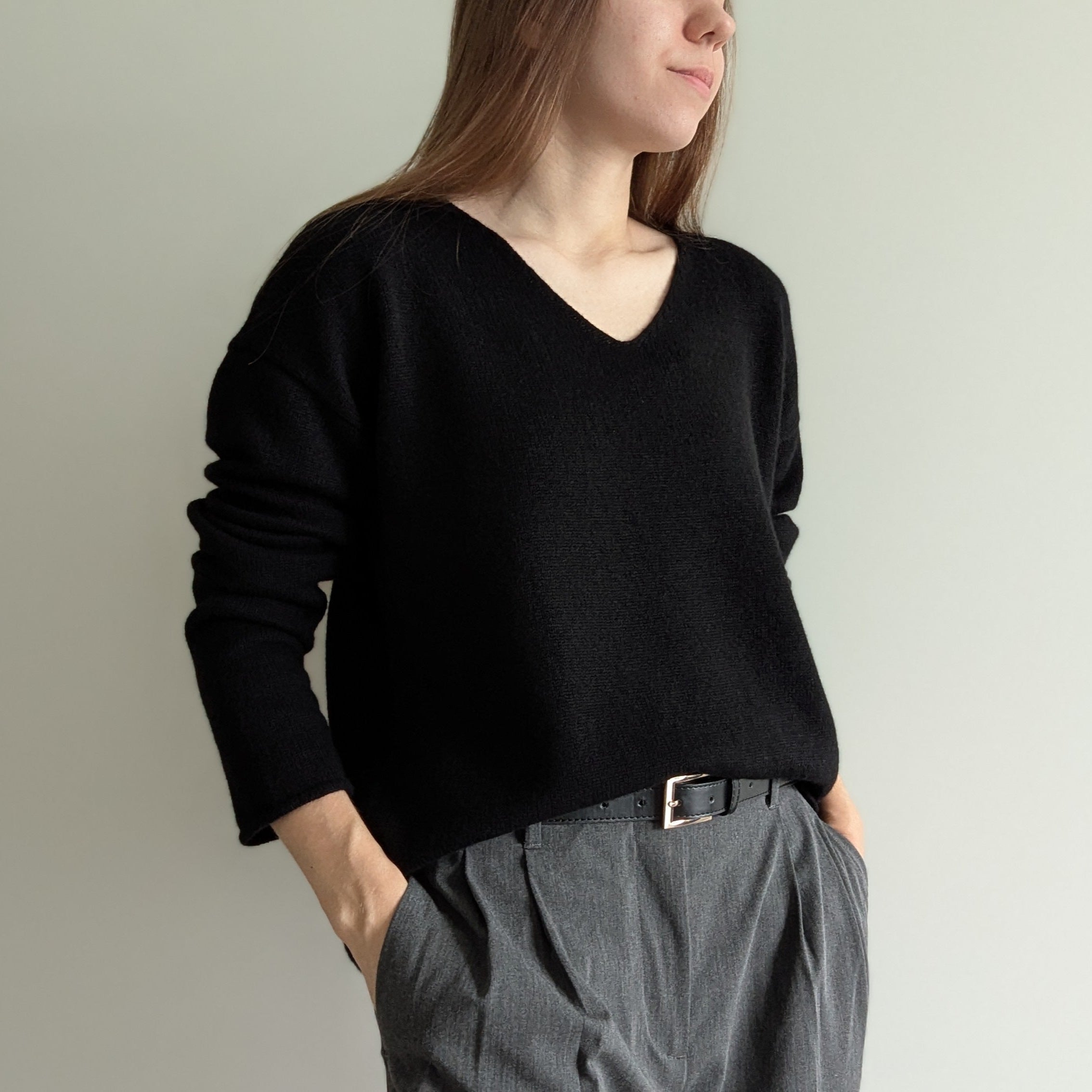 Black Person wearing a black sweater and gray pants against a plain background