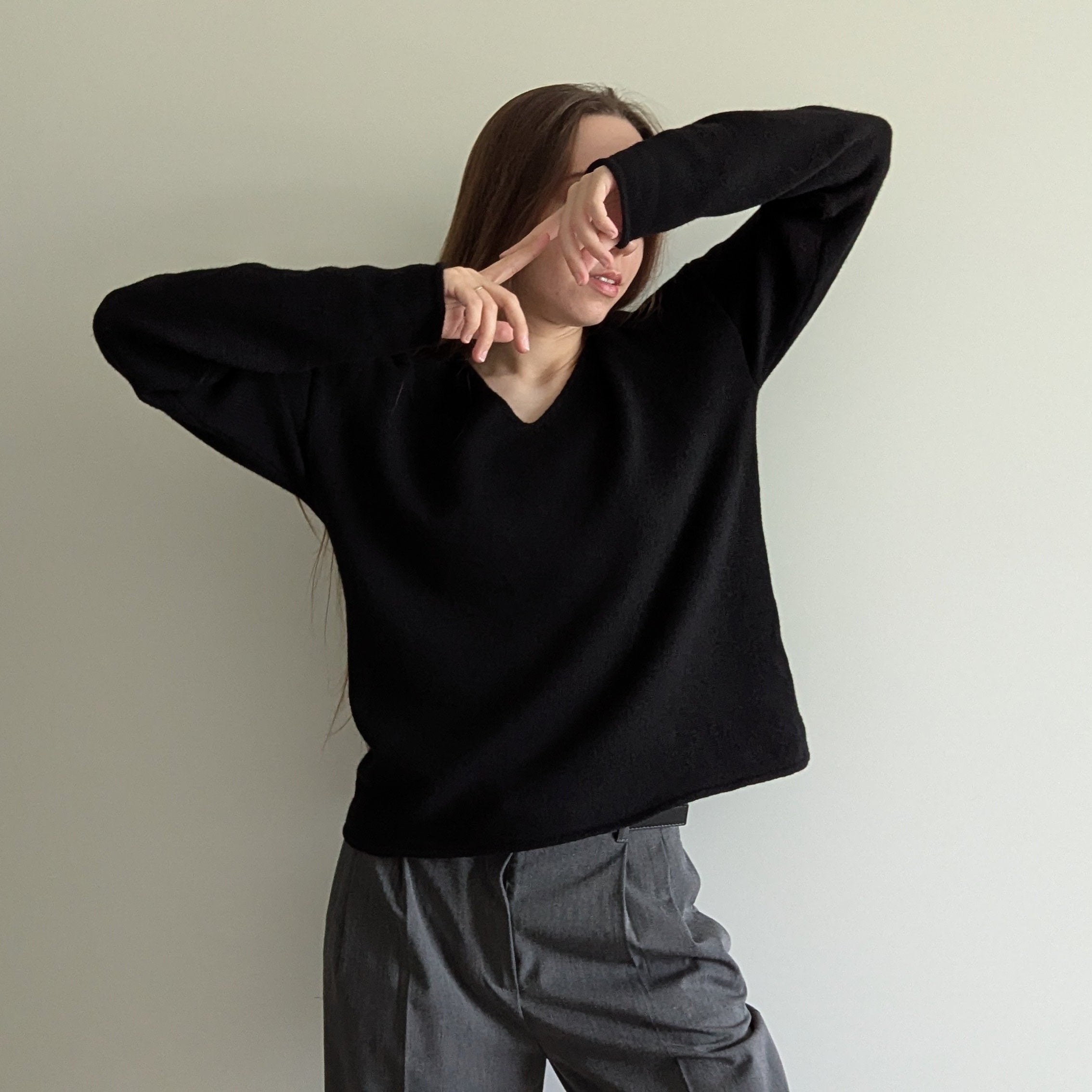 Black Person wearing a black sweater and gray pants against a plain background