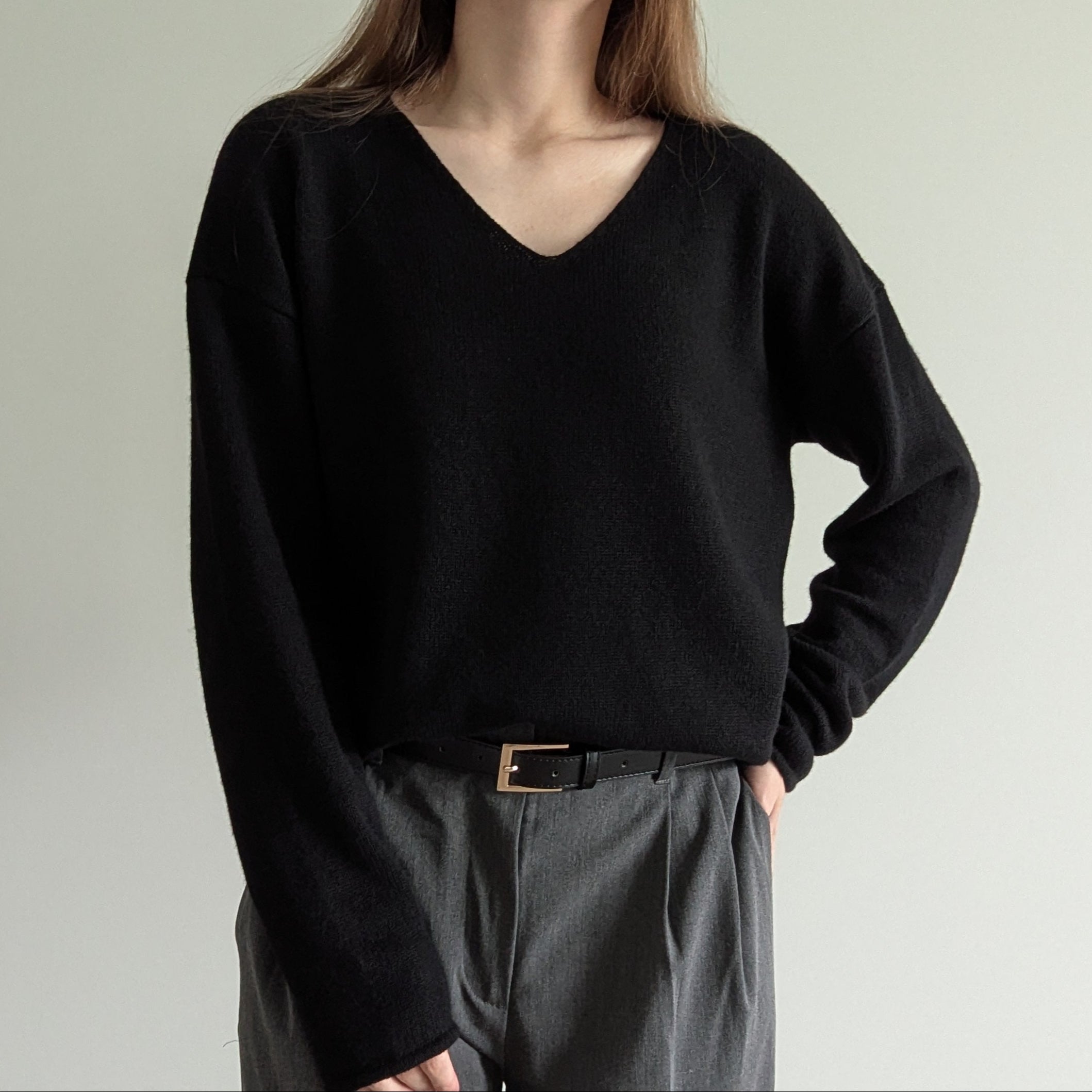 Black Person wearing a black sweater and gray pants against a plain background