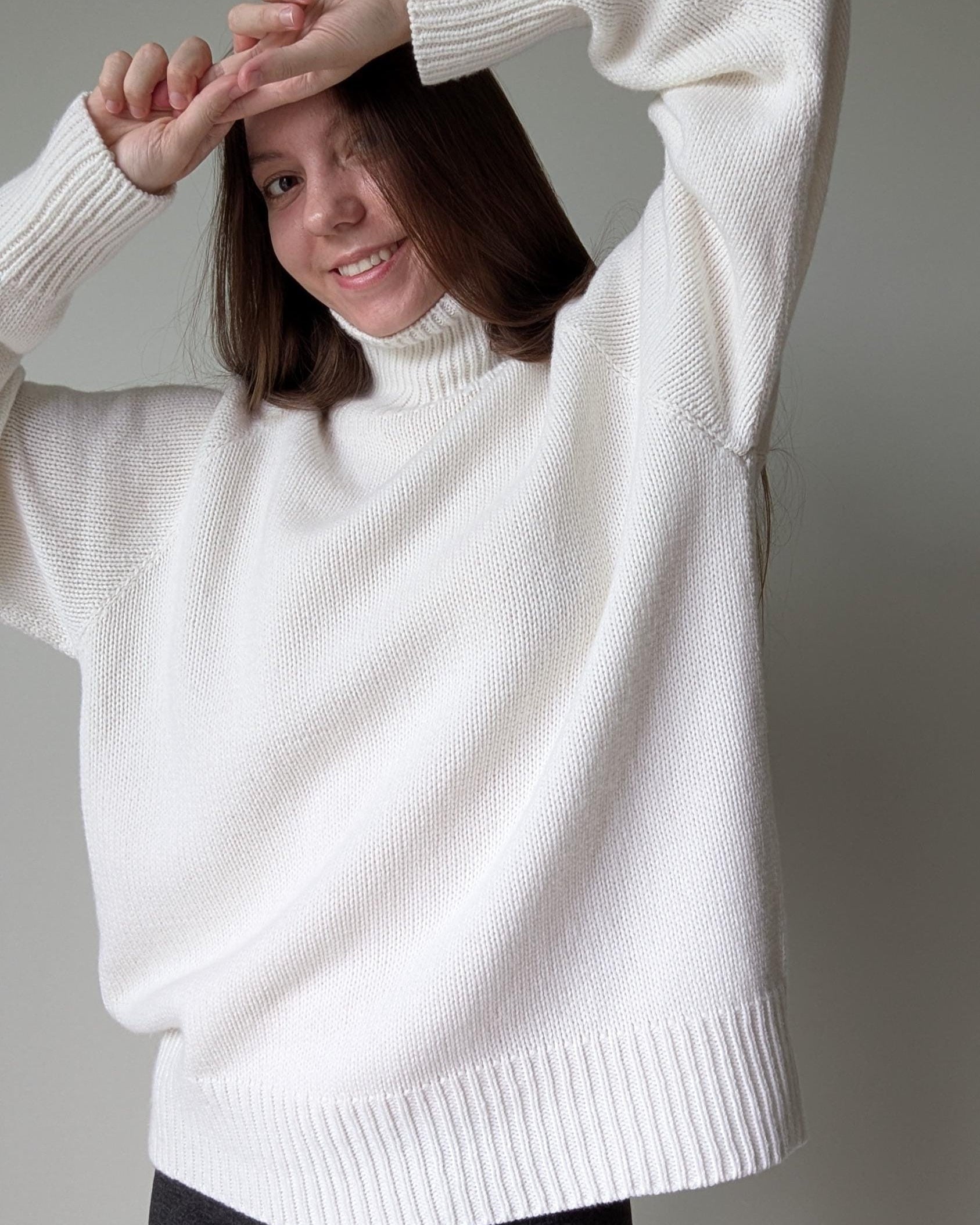 White Person wearing a white sweater against a plain background