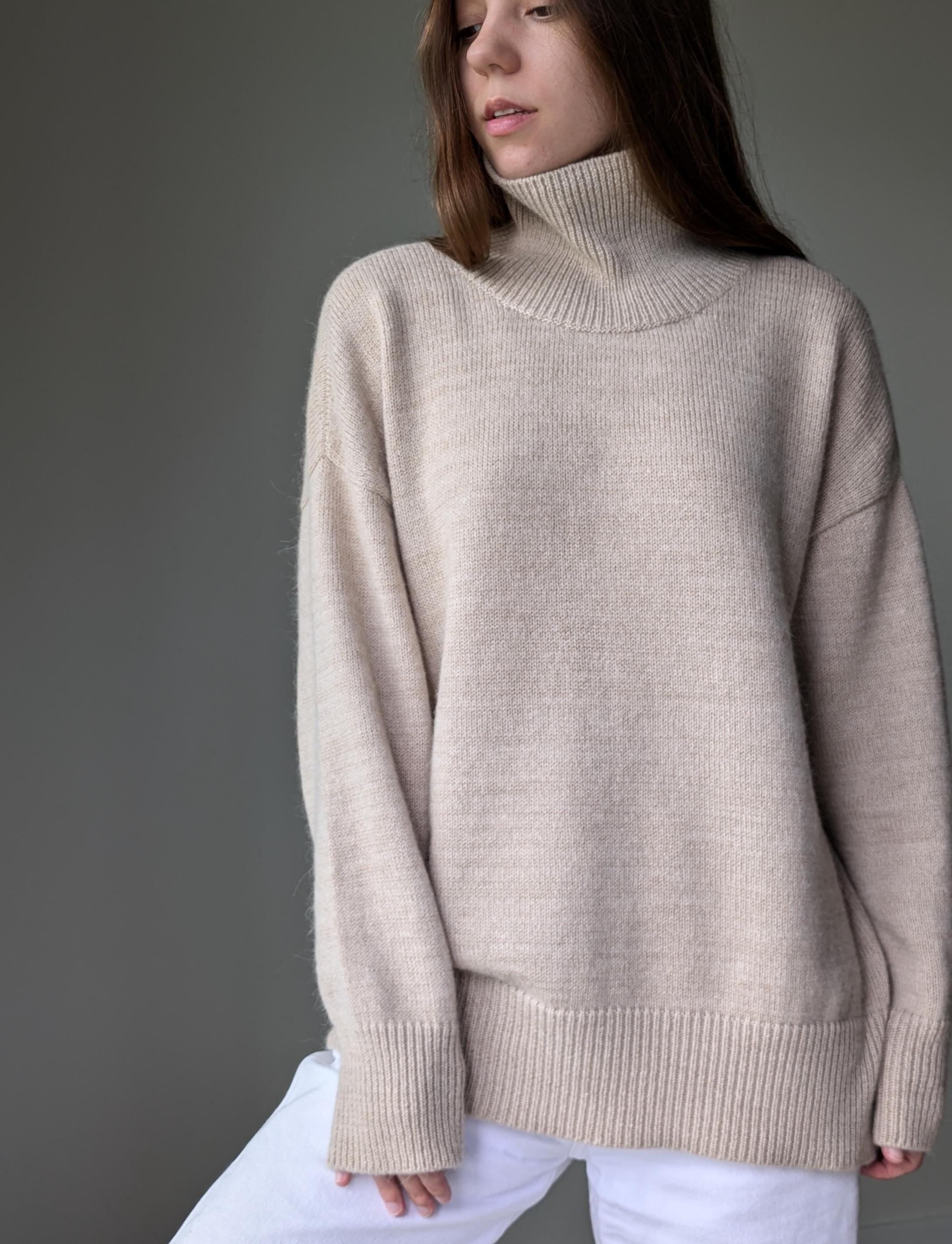 Sand person wearing a beige turtleneck sweater against a gray background