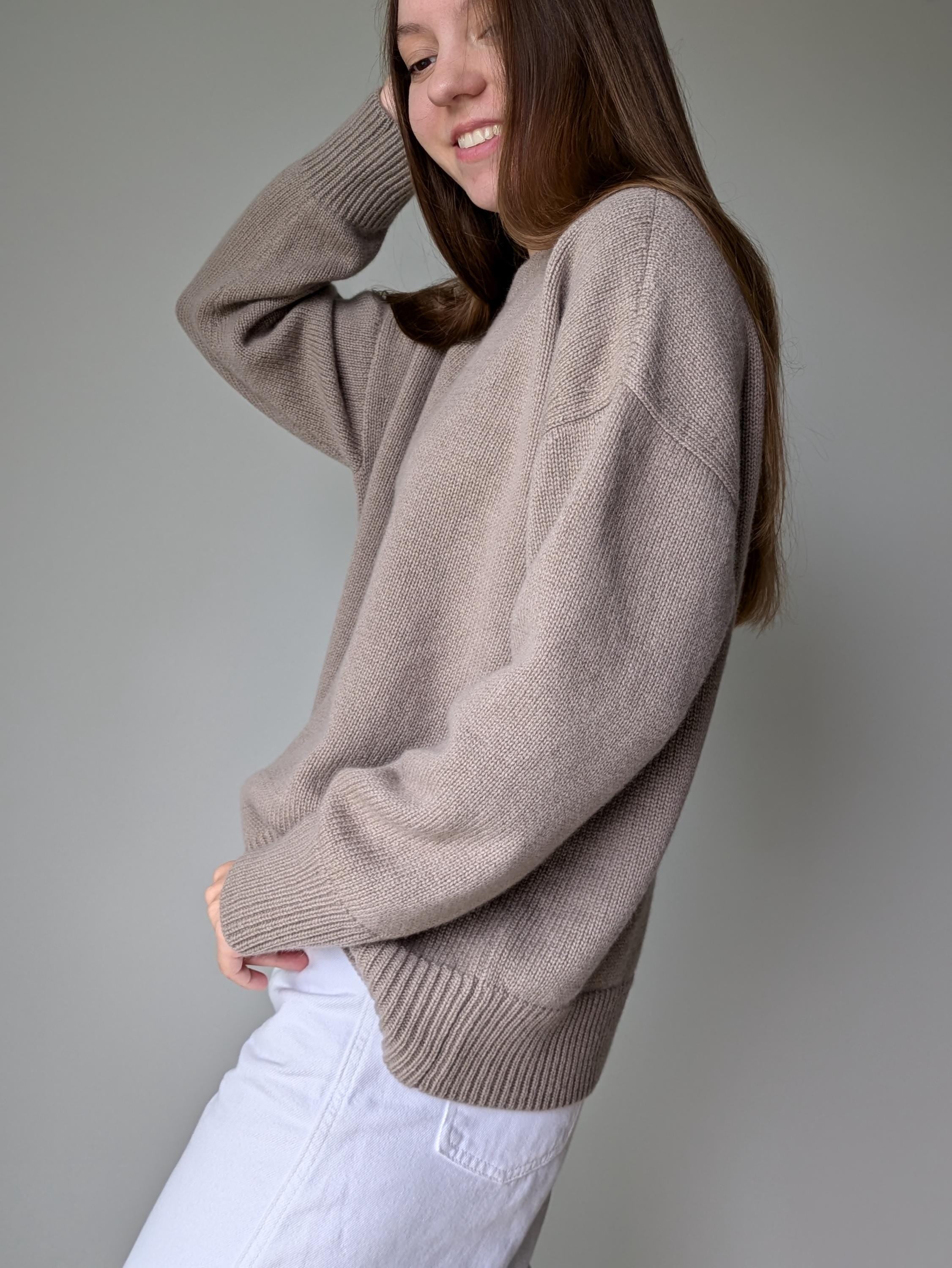 Person wearing a beige sweater and white pants against a plain background