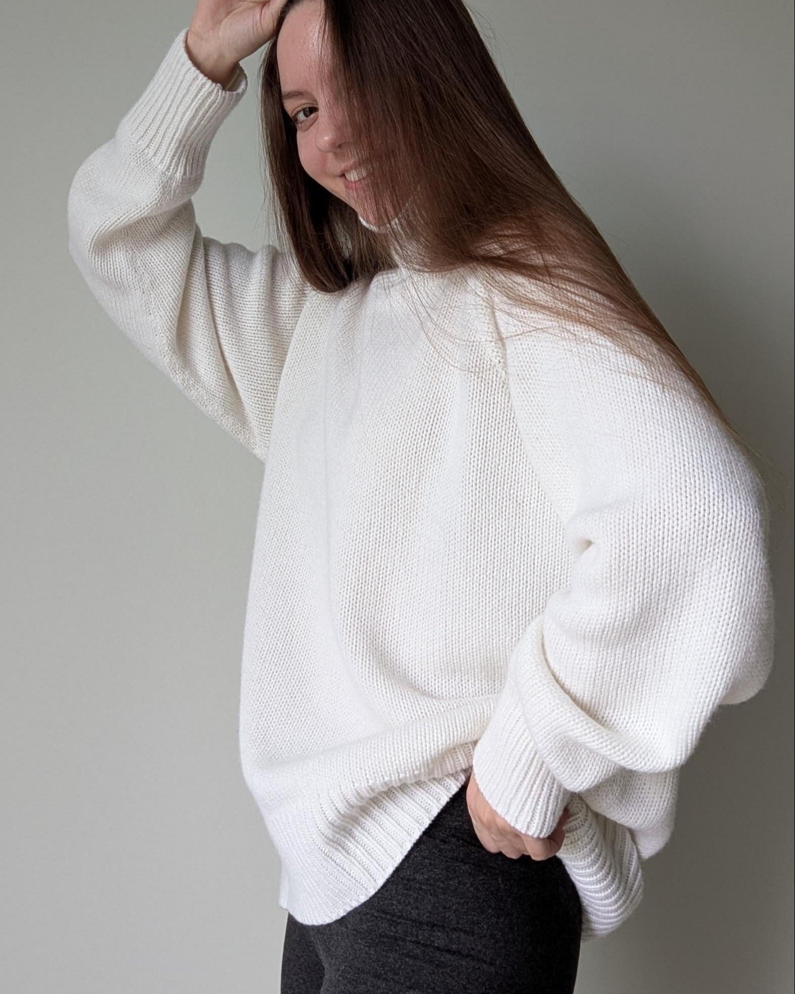 White Person wearing a white sweater against a plain background