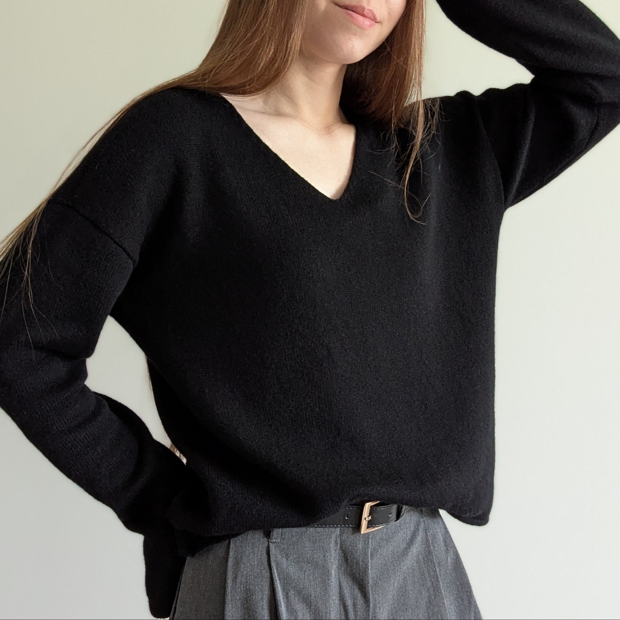 Black Person wearing a black sweater and gray pants on a plain background
