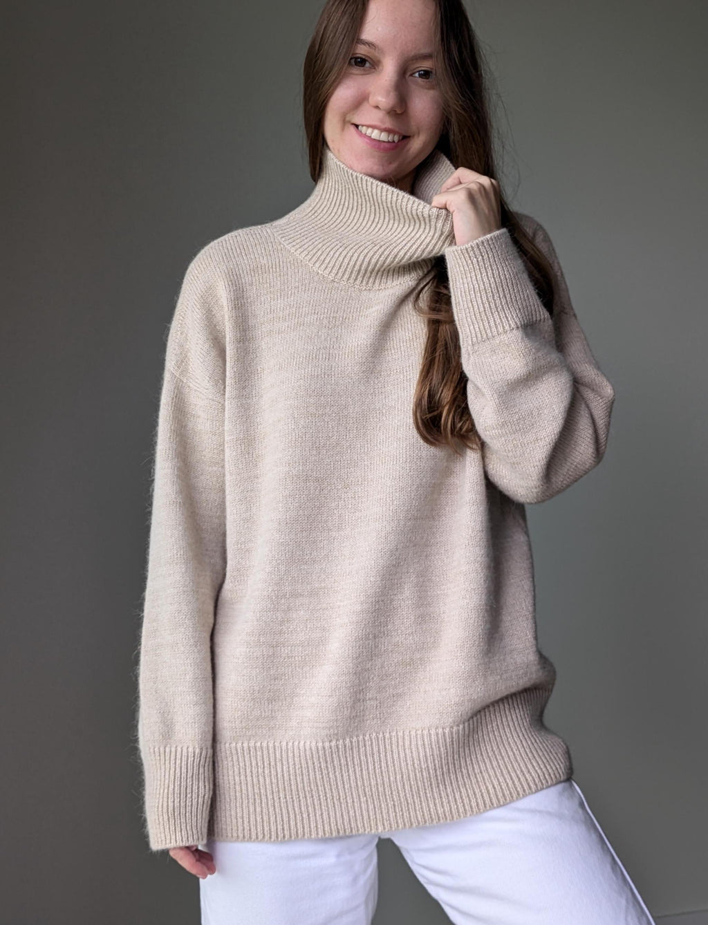 Sand woman wearing a beige turtleneck sweater against a gray background