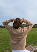 Person wearing a beige sweater standing in a grassy field with trees in the background