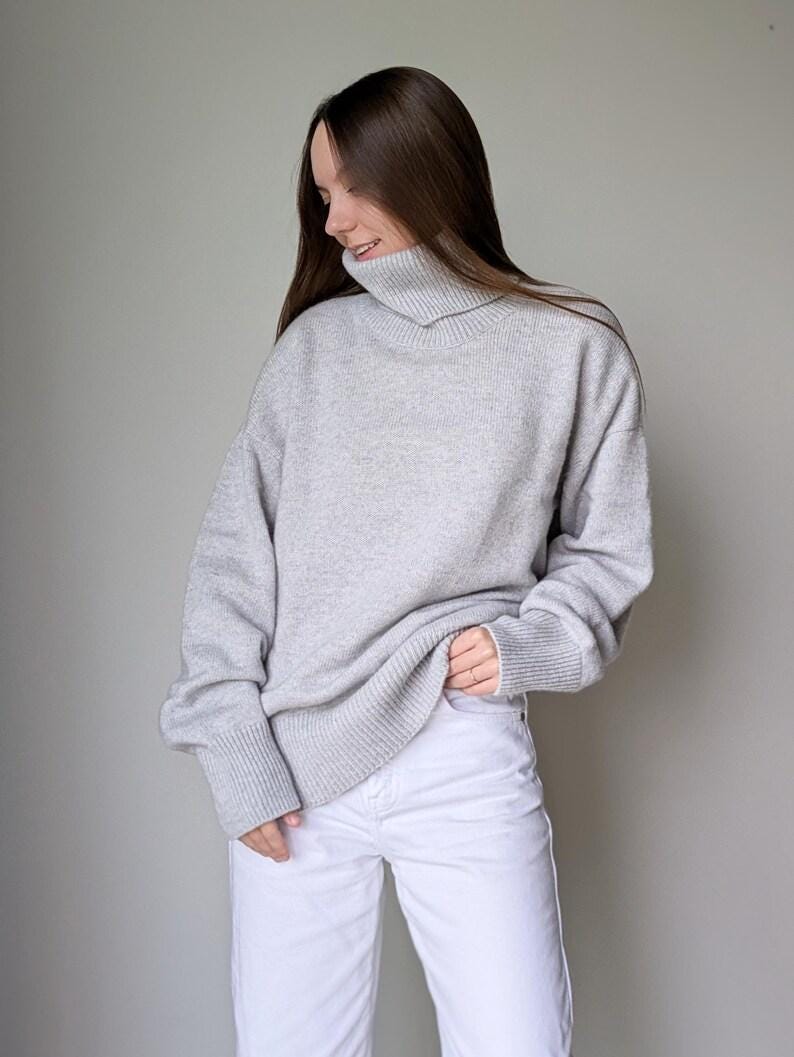 Pearl gray Person wearing a gray sweater and white pants against a plain background