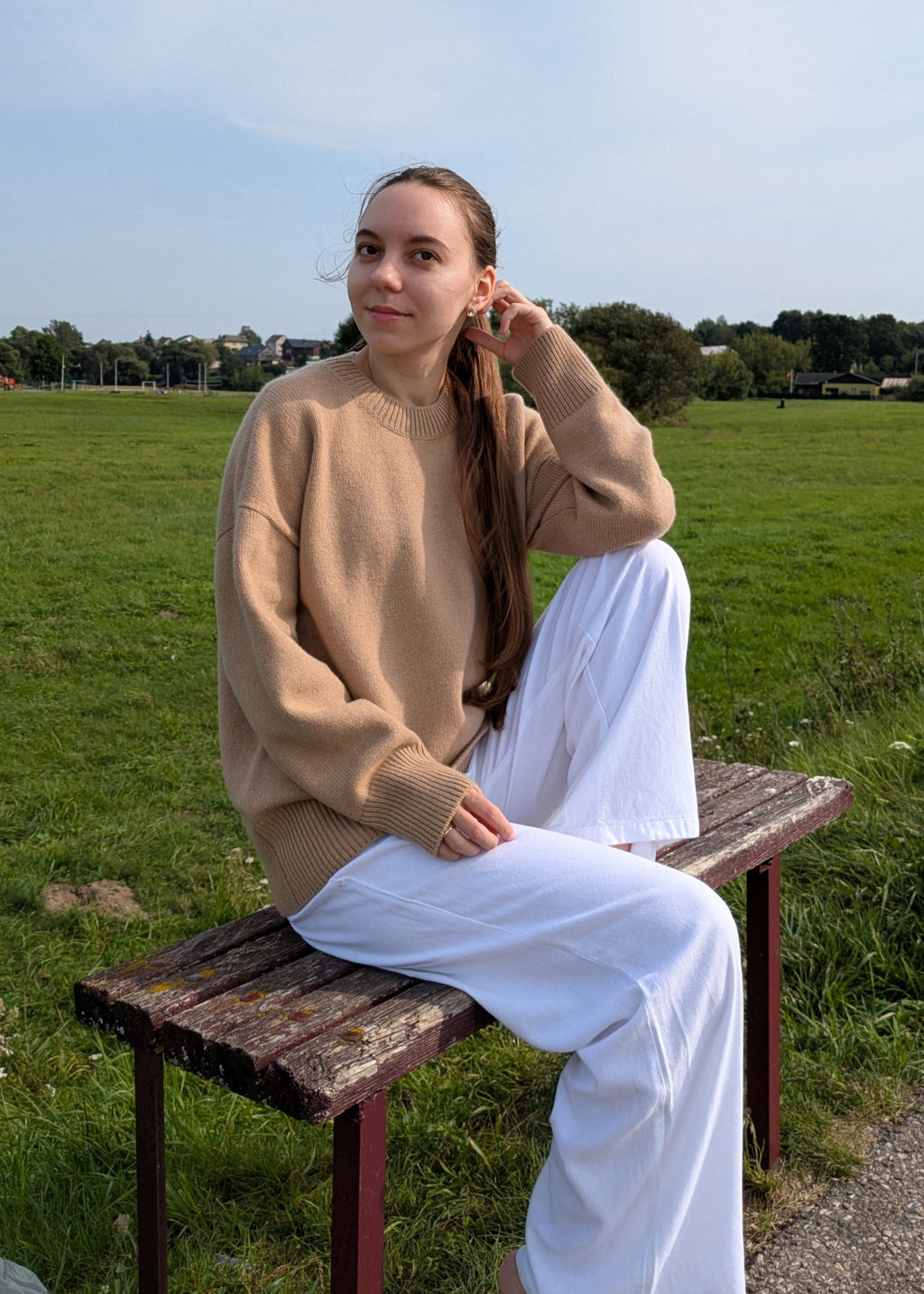 Woman sitting on a wooden bench in a grassy field