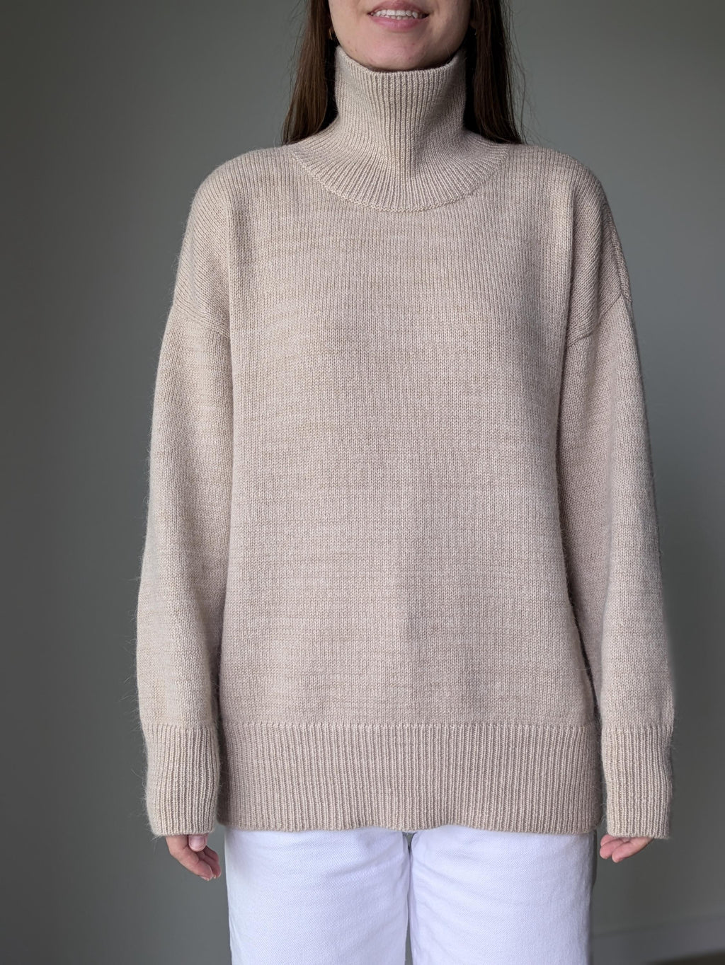 Sand person wearing a beige turtleneck sweater against a gray background