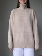Sand person wearing a beige turtleneck sweater against a gray background
