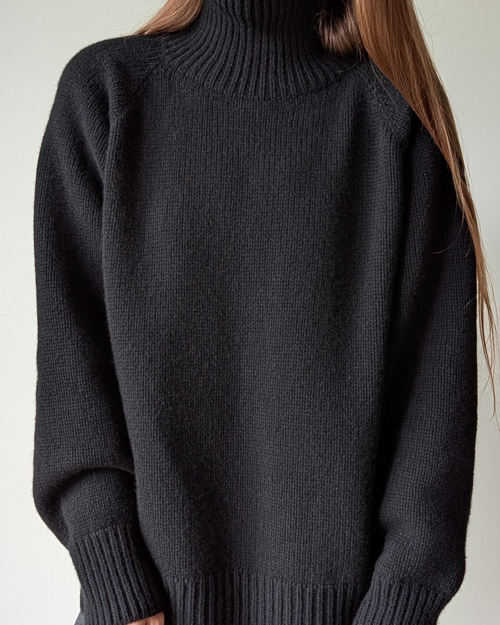 Black sweater worn by a person against a neutral background