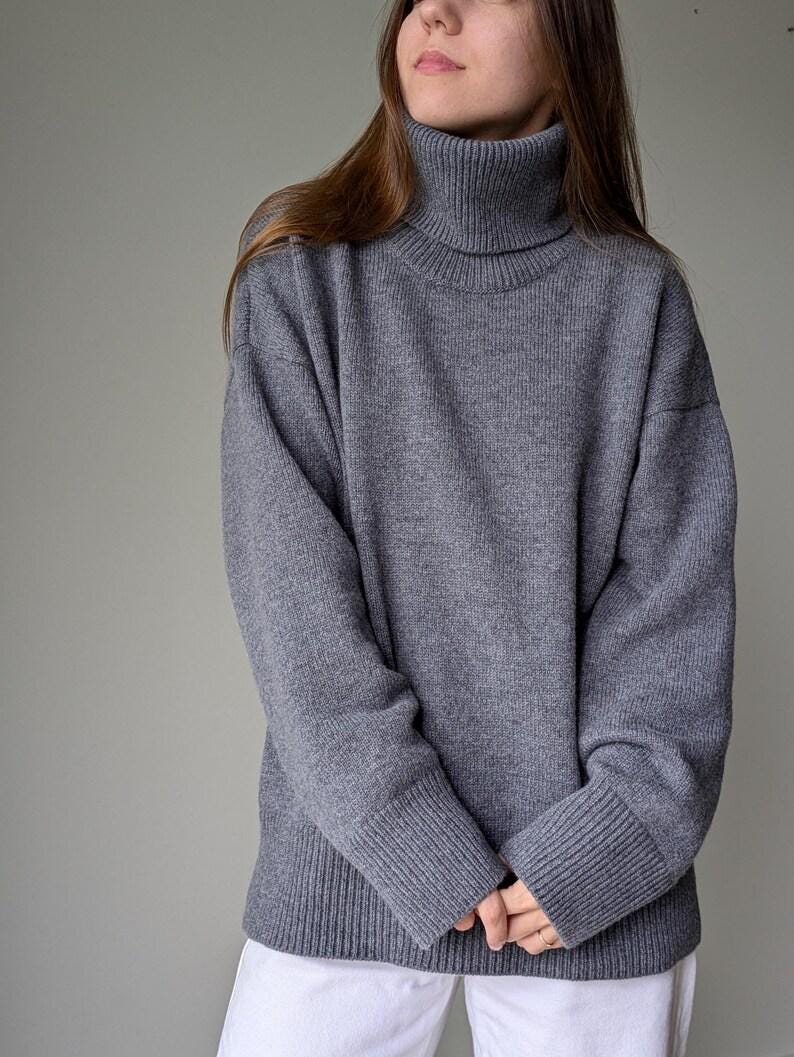 Gray Person wearing a gray turtleneck sweater against a plain background