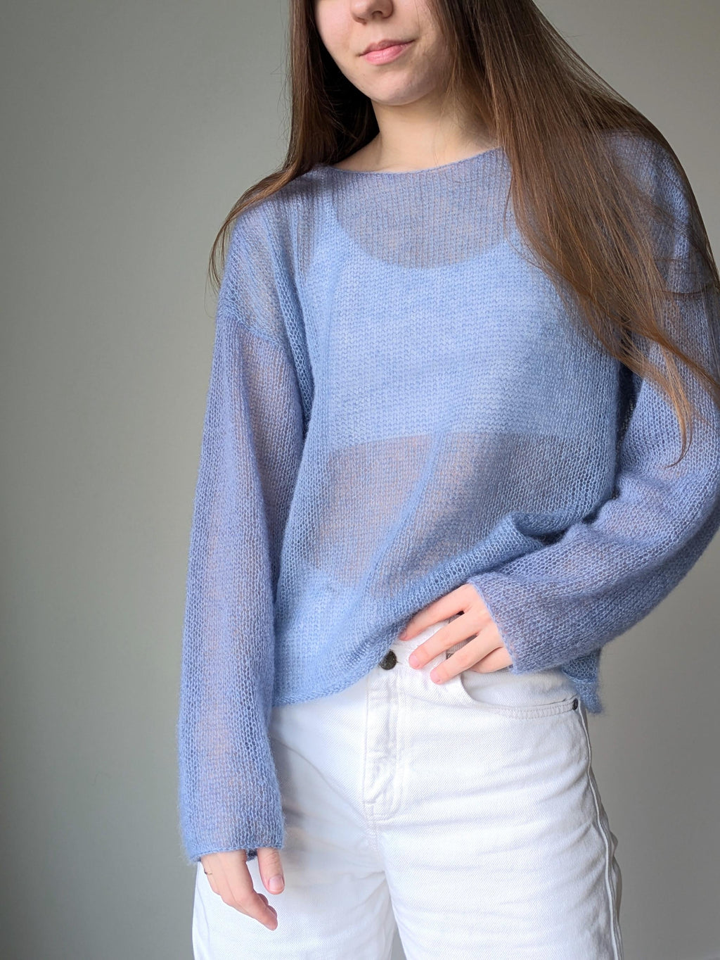 Person wearing a light blue sweater and white pants against a gray background