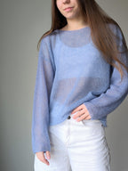 Person wearing a light blue sweater and white pants against a gray background