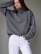 Gray Person wearing a gray turtleneck sweater and white pants against a plain background