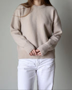 Person wearing a beige sweater and white pants against a gray background