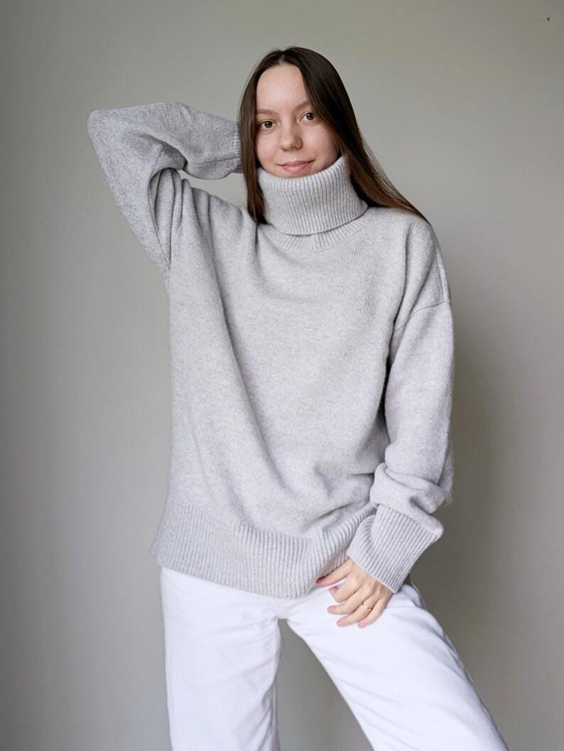 Pearl gray Woman wearing a gray sweater and white pants against a plain background