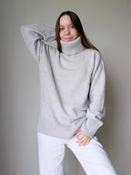 Pearl gray Woman wearing a gray sweater and white pants against a plain background