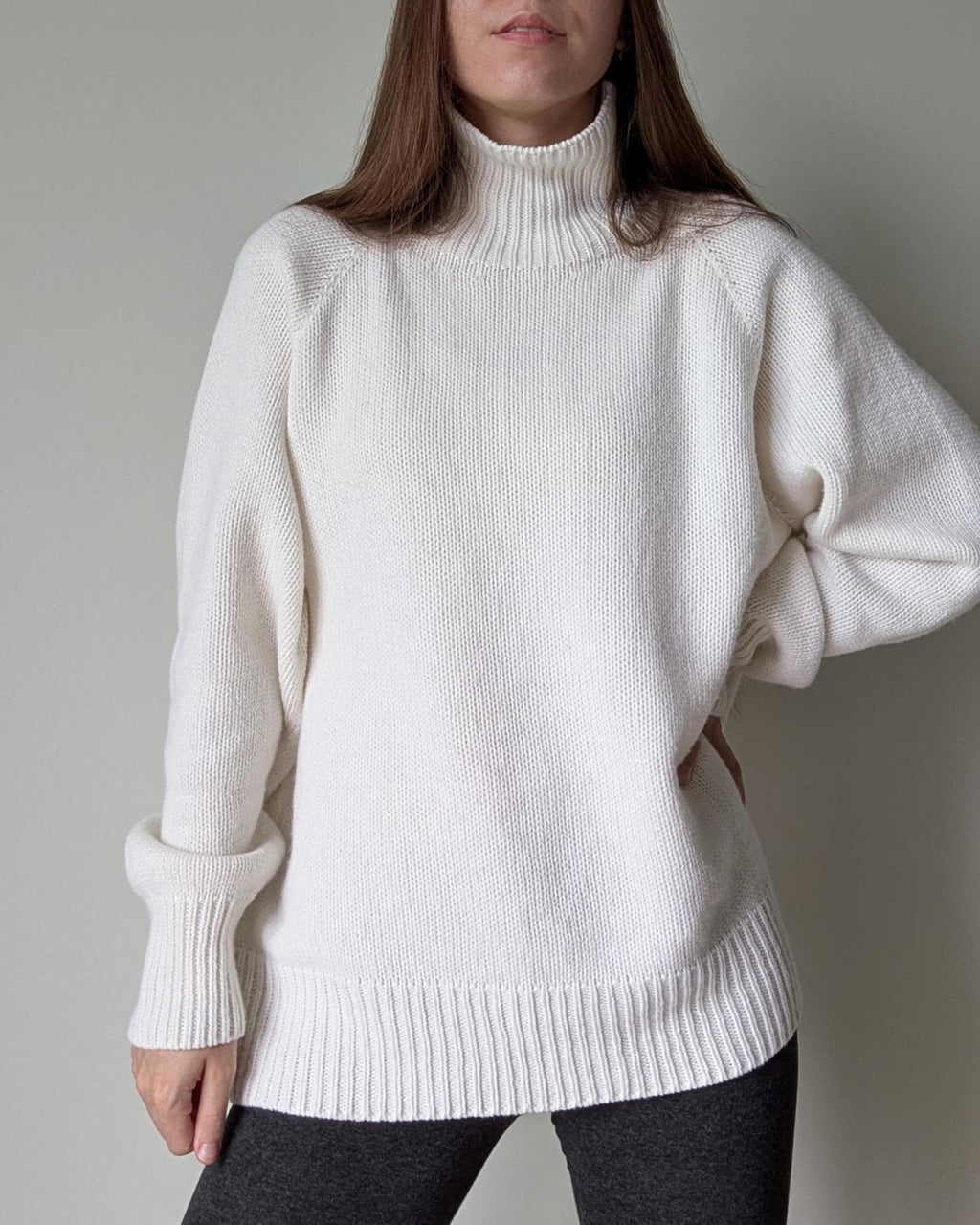 White Person wearing a white turtleneck sweater against a plain background