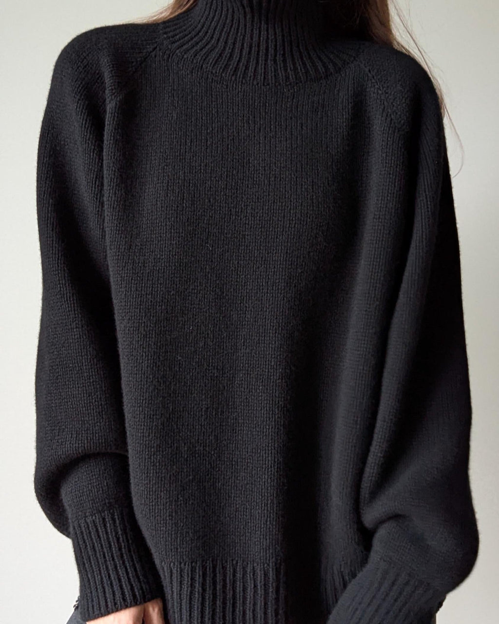 Black turtleneck sweater worn by a person on a plain background