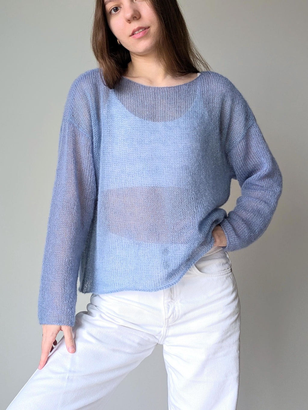 Ocean woman wearing a light blue sweater over a sheer top with white pants against a plain background