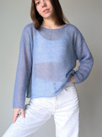 Ocean woman wearing a light blue sweater over a sheer top with white pants against a plain background