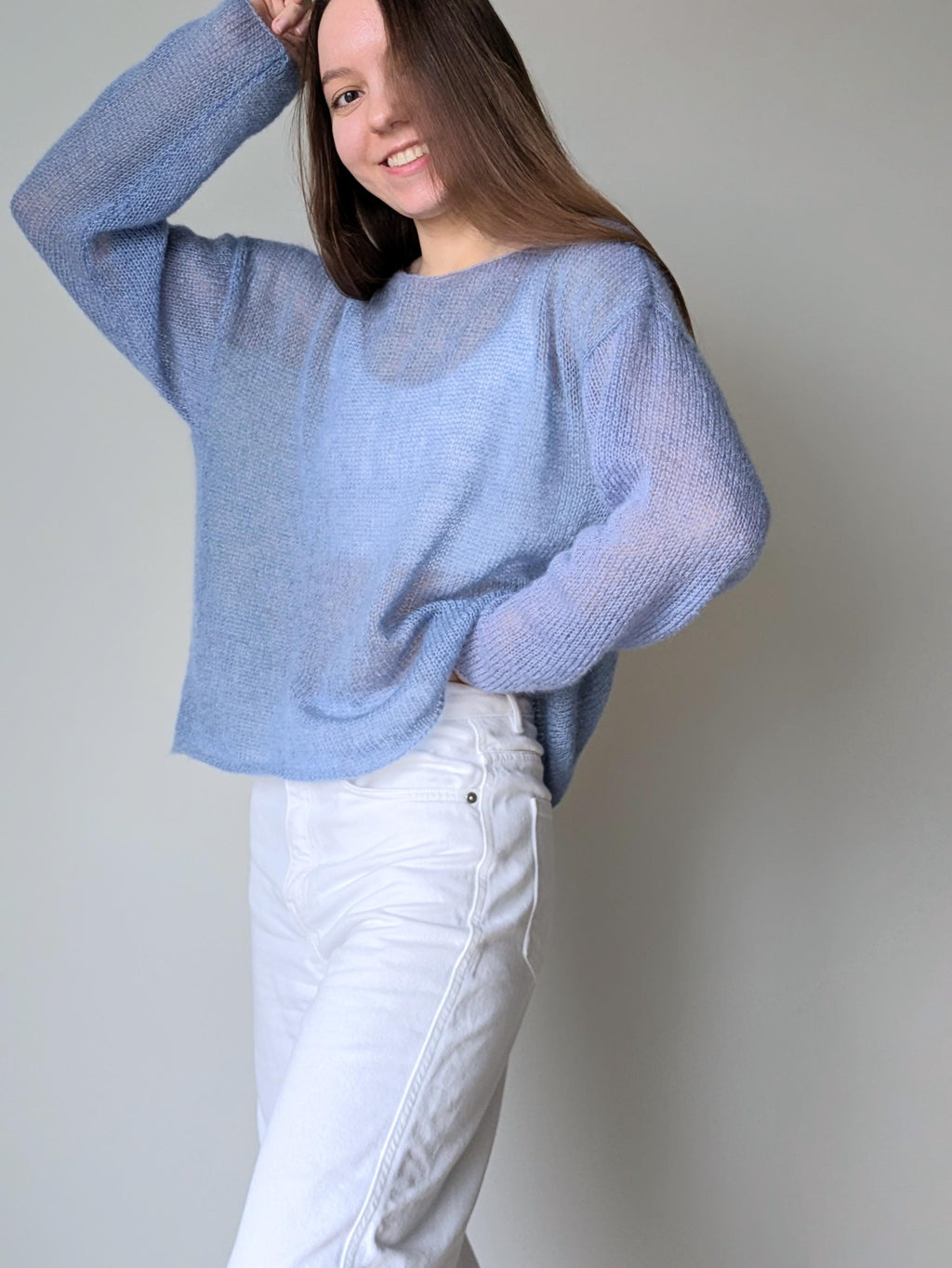 Person wearing a light blue sweater and white pants against a plain background