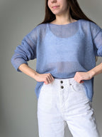 Person wearing a blue sweater and white pants against a gray background